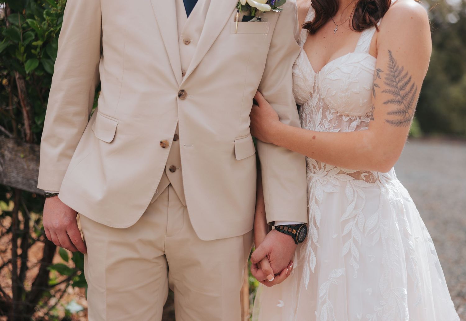 Wedding party in beige suits and white gown pose together in garden setting.