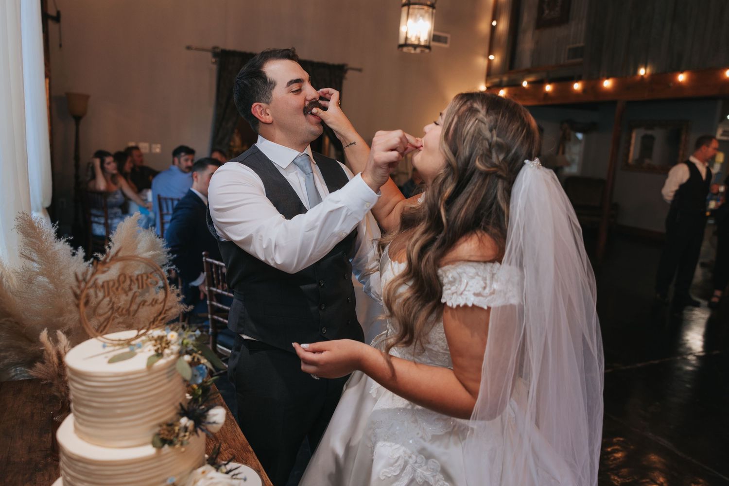 Wedding reception celebration with string lights and guests dancing in a dimly lit indoor venue.