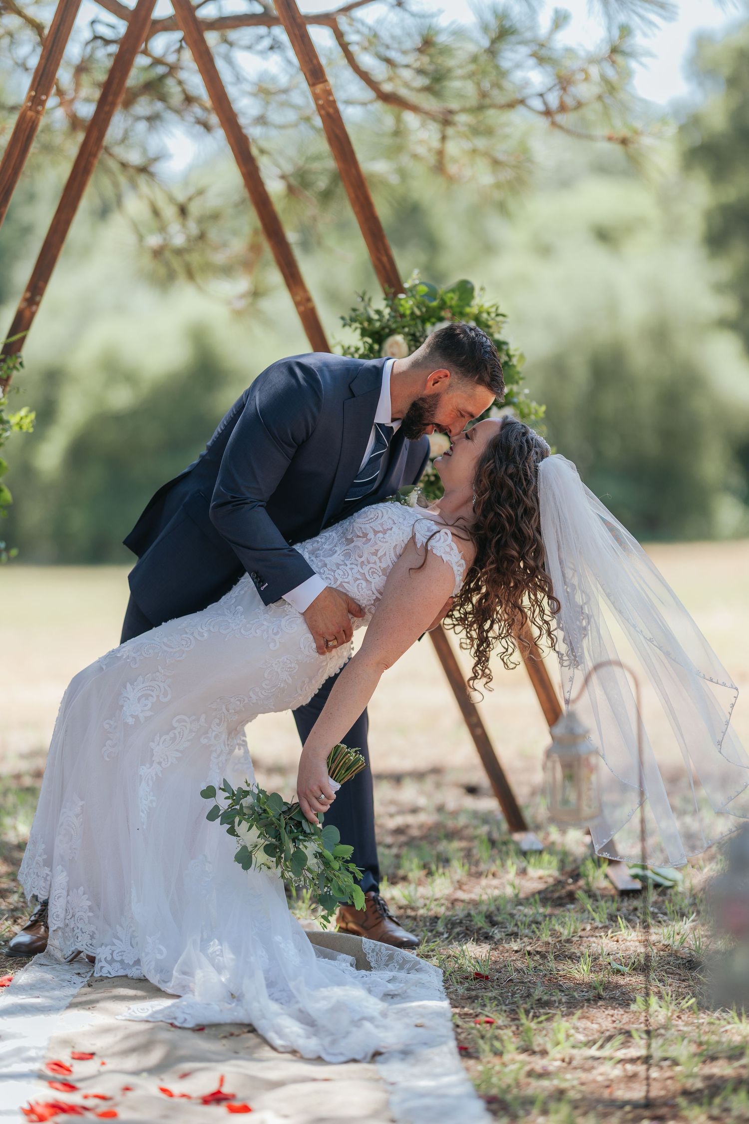 Romantic wedding couple posing under wooden triangle arch with floral decorations.