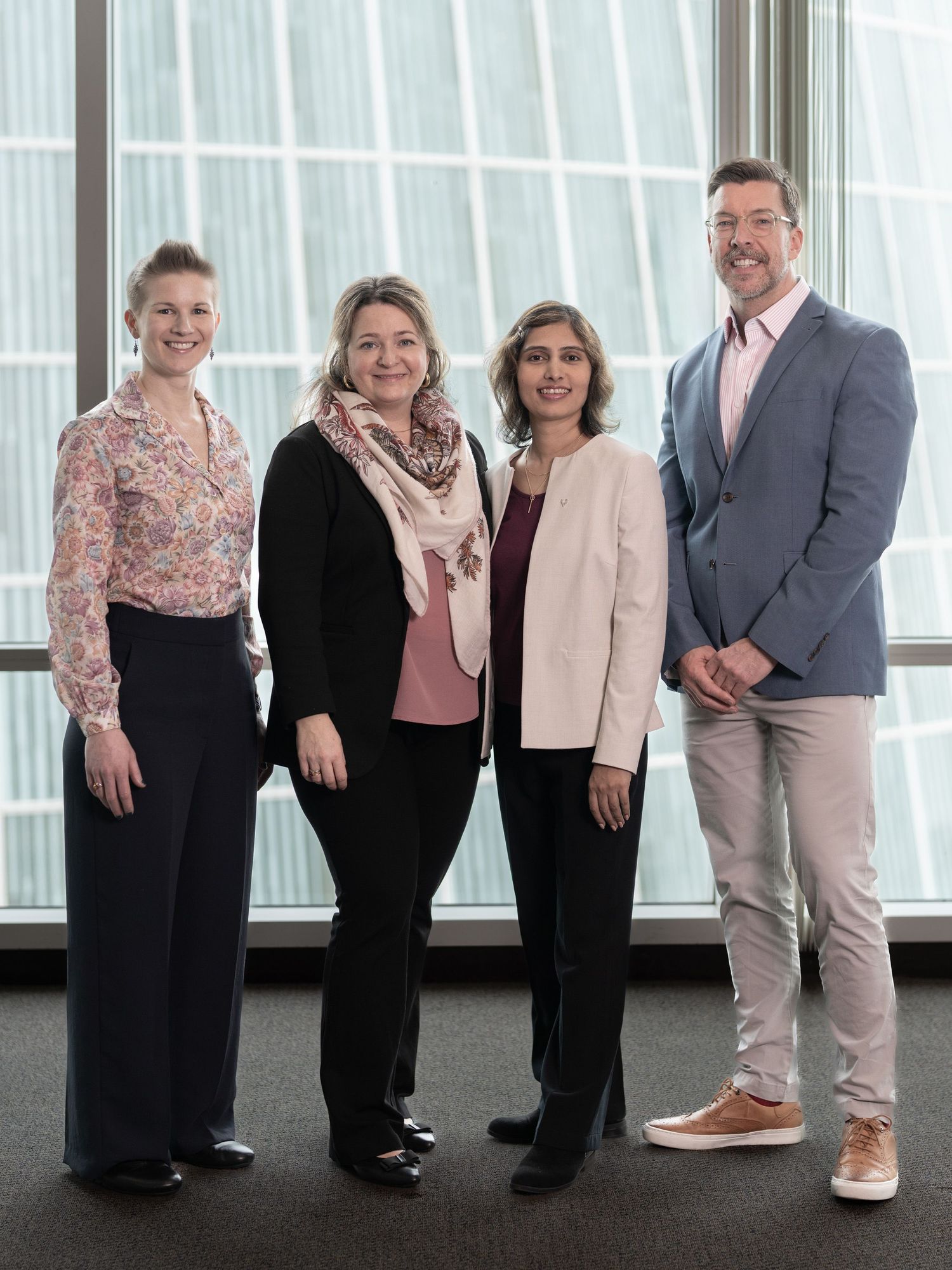 Four business professionals smiling and posing together in a modern office building with large windows.