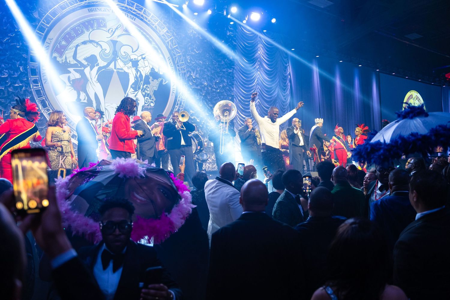 Lively Mardi Gras celebration with performers, colorful feathered hats, and vibrant stage lighting at an elegant gala event.