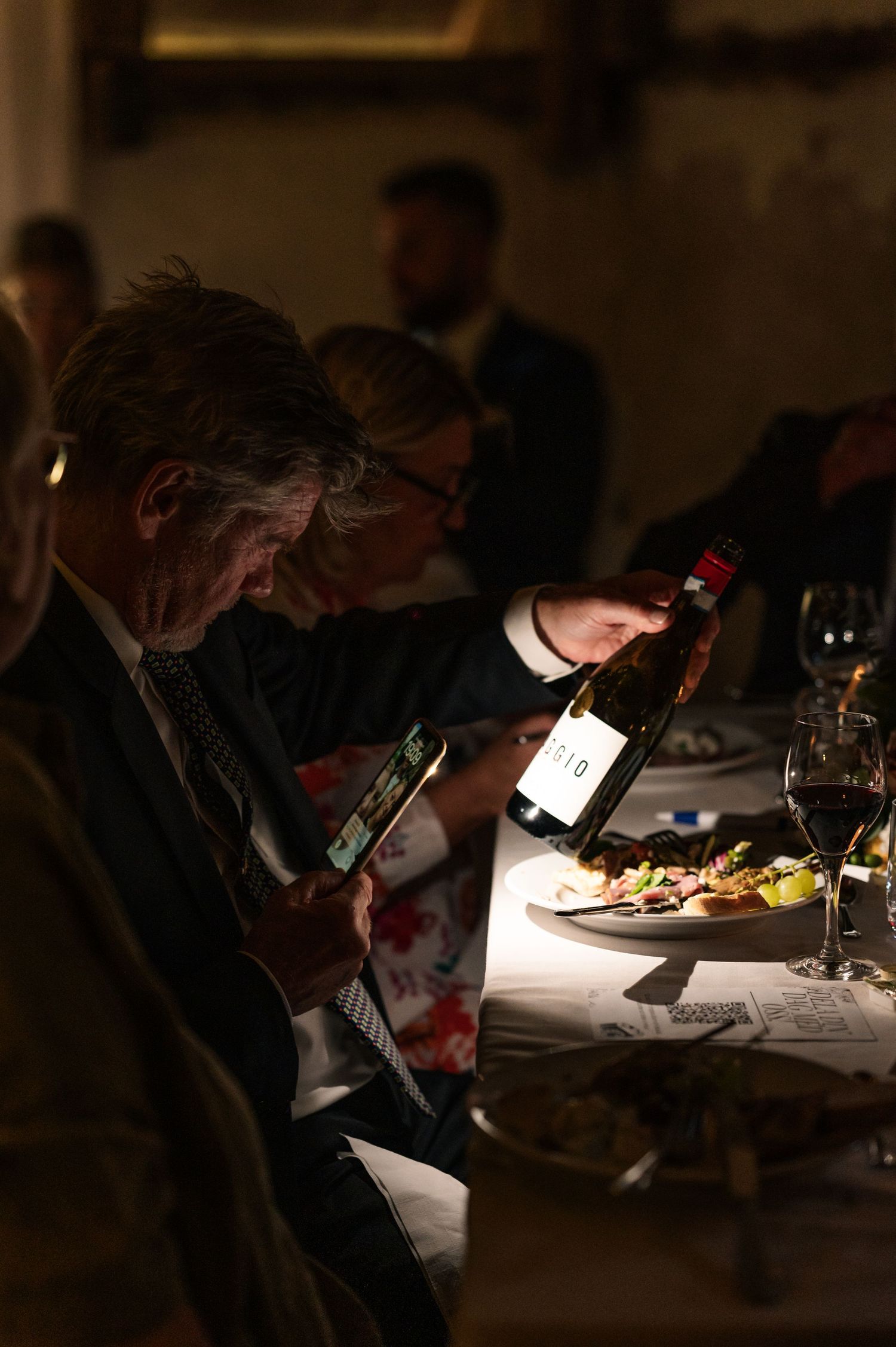 Guest examines wine bottle in dimly lit reception dinner setting.