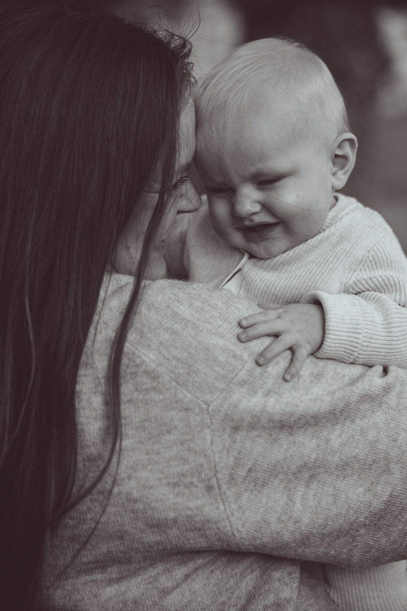 Black and white photo of a mother holding her laughing baby close, sharing a tender moment of joy.