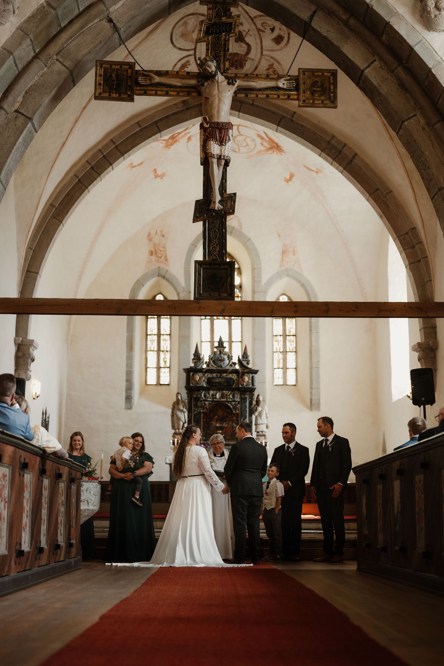 Bride and groom exchange vows at a historic church altar with red carpet aisle and gothic arched ceiling.