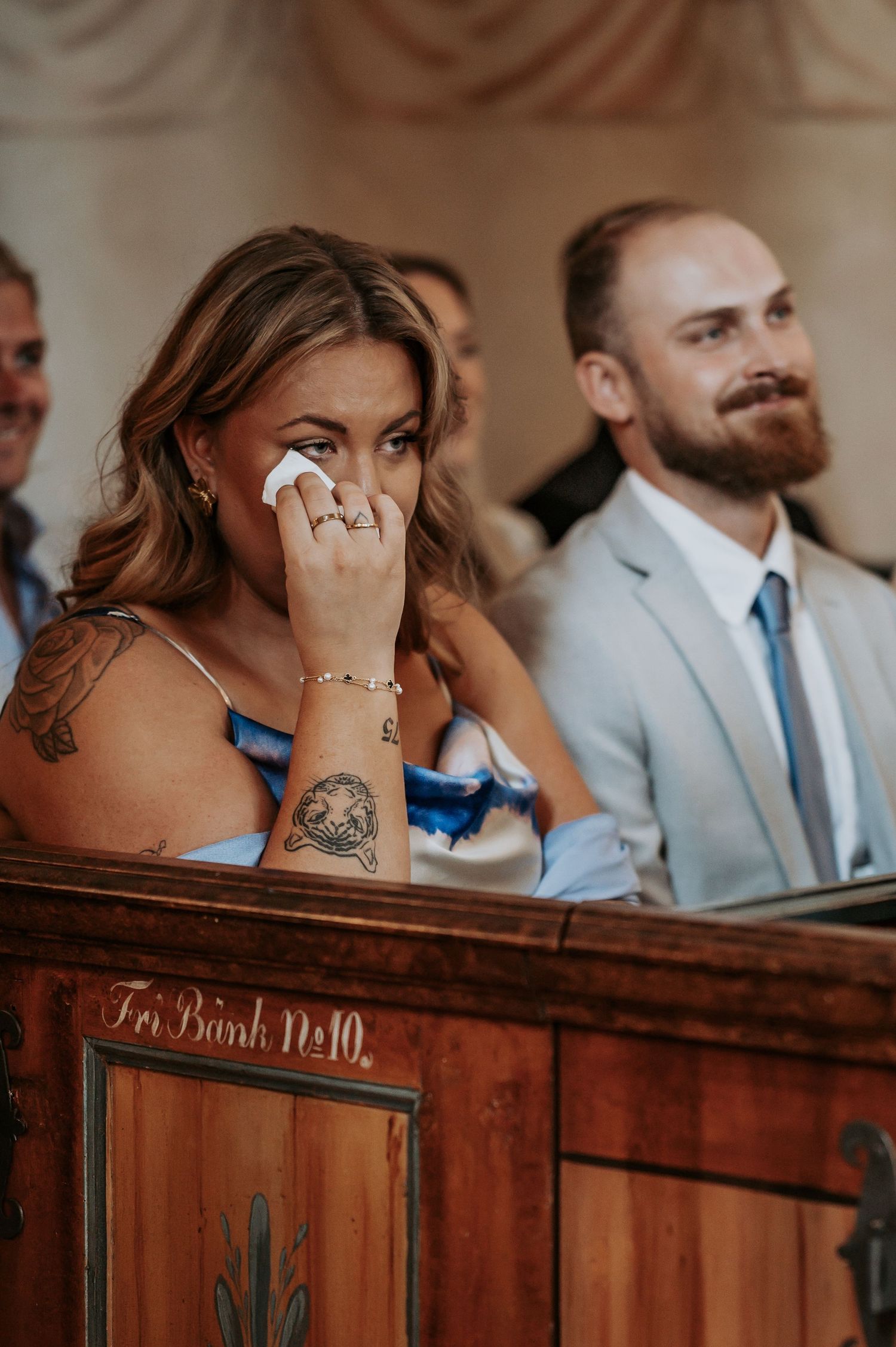 Emotional wedding guest wipes tears during ceremony in wooden church pew.
