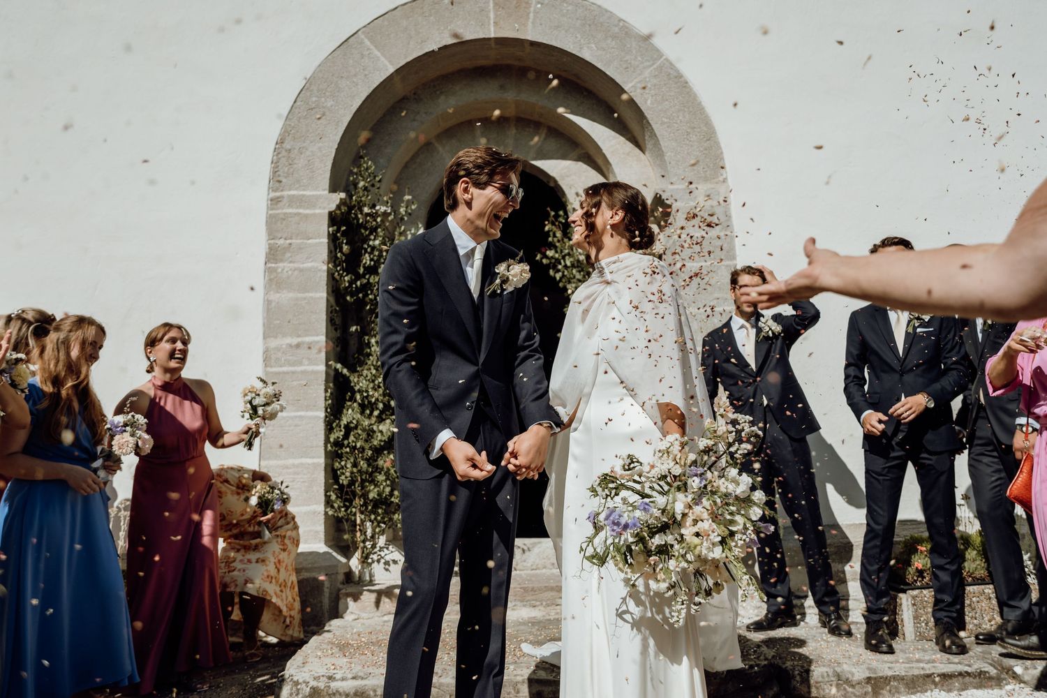 Wedding guests celebrate by tossing flower petals at a joyous outdoor ceremony.