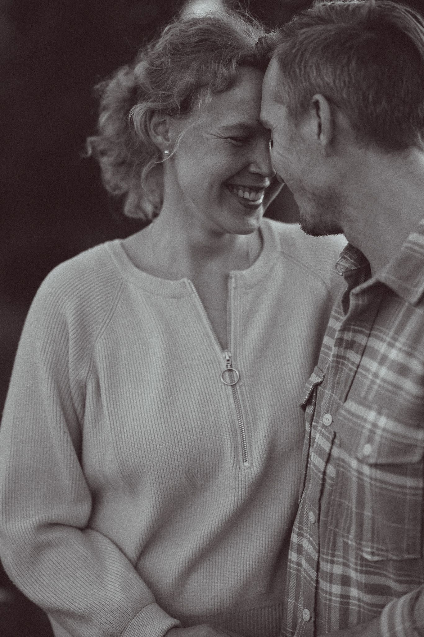 Black and white photo of a laughing couple leaning foreheads together, woman in ribbed sweater, man in plaid shirt.