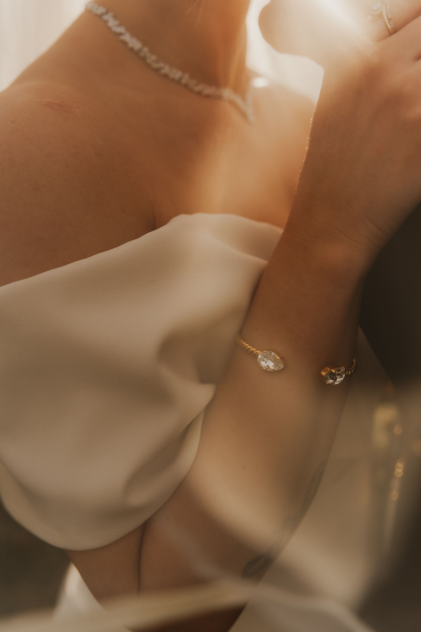Close-up of a bride wearing a diamond bracelet, delicate necklace, and elegant white strapless gown in warm golden light.
