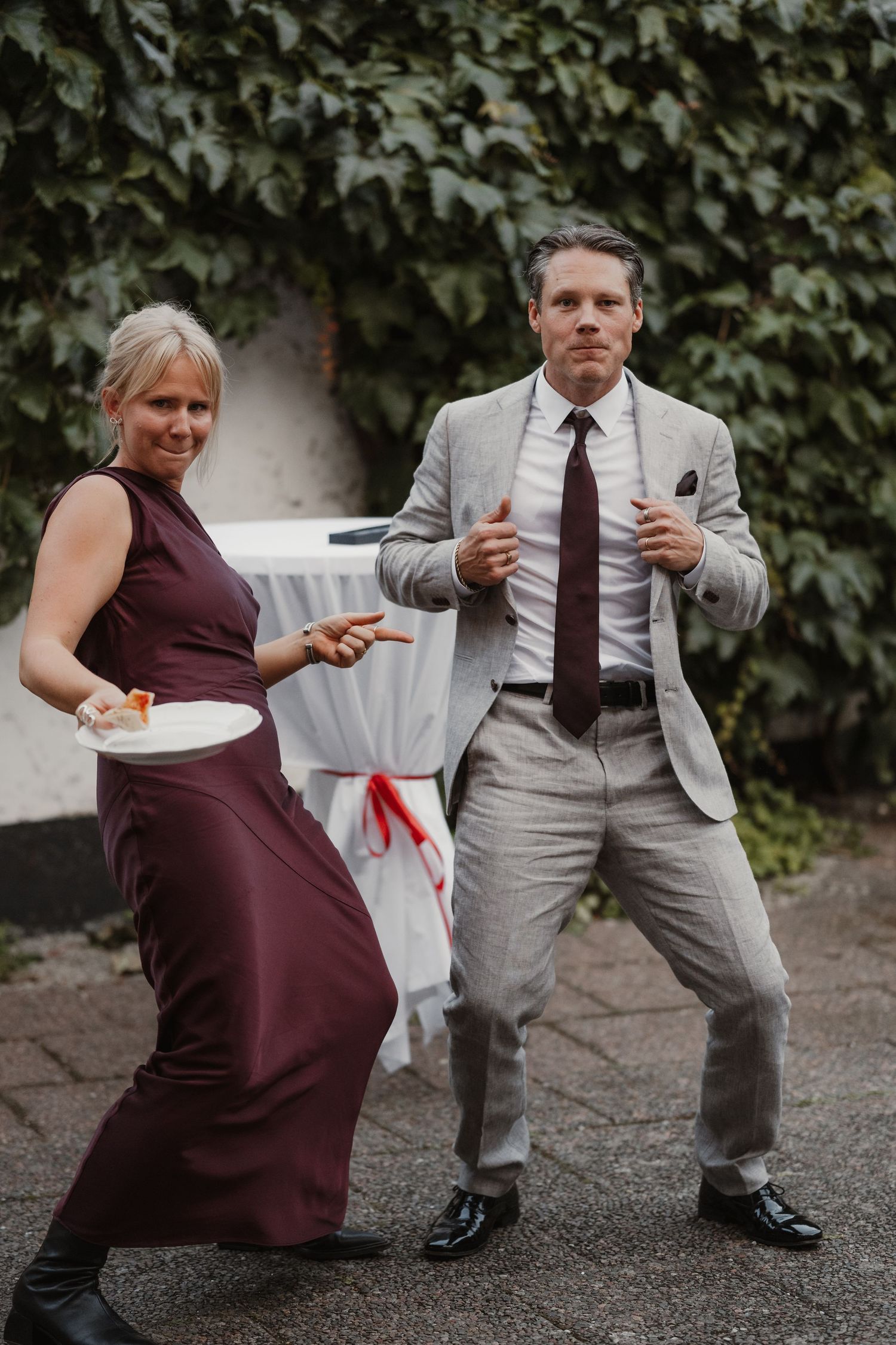 A couple in burgundy dress and gray suit playfully share fast food in a series of candid outdoor photos.