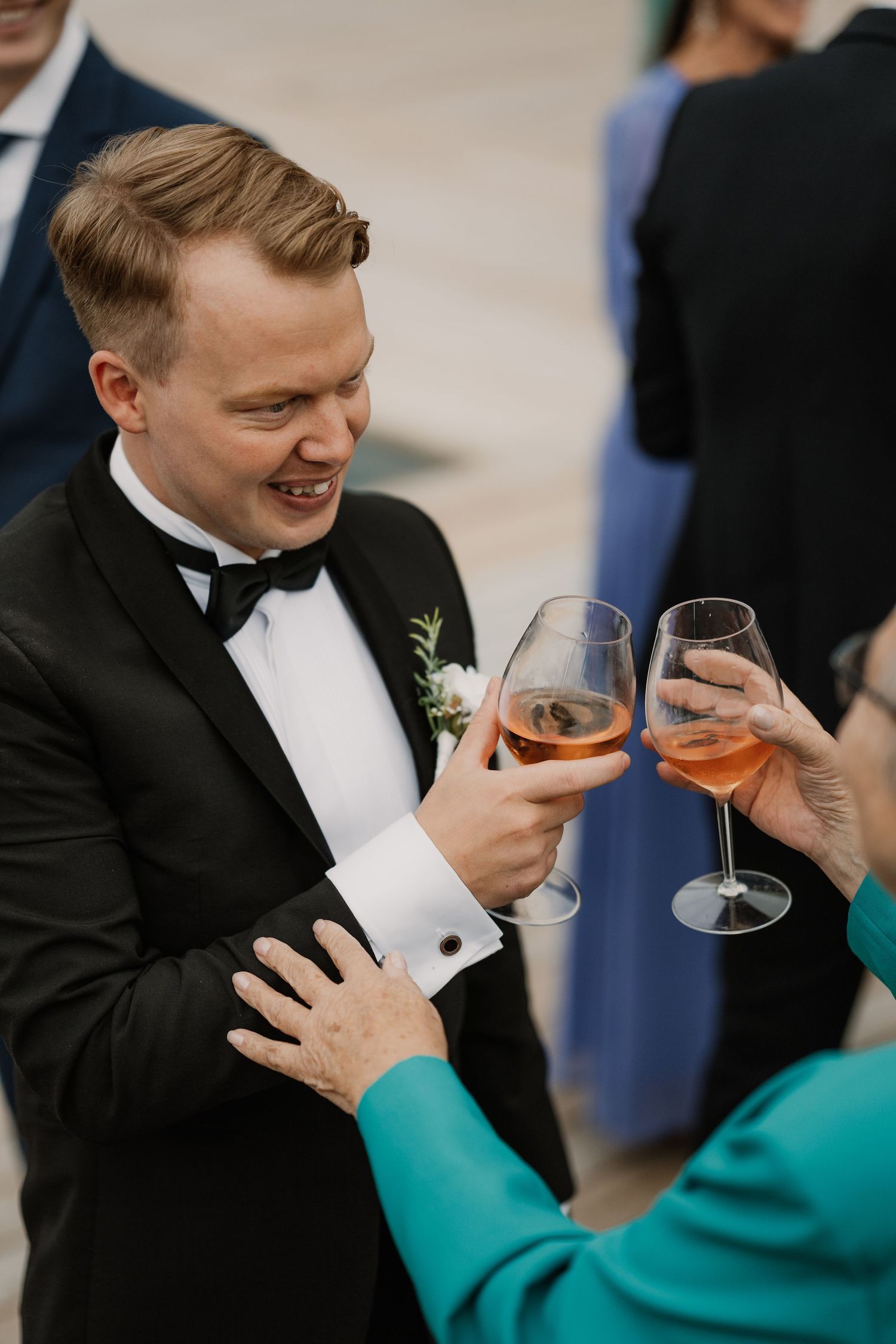 A guest in a black tuxedo and bow tie toasts with wine glasses at a formal celebration event.