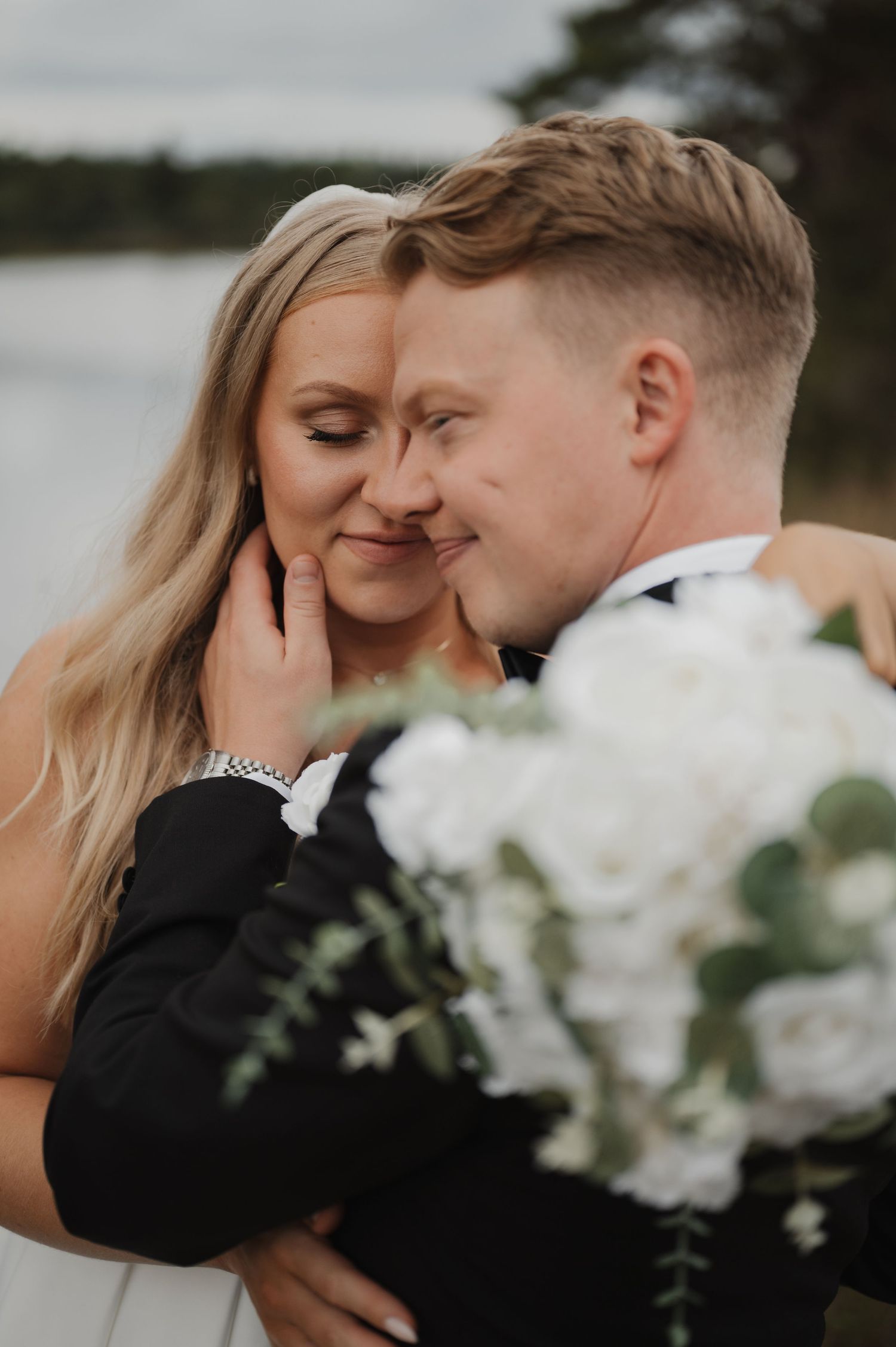 A romantic moment captured between a couple with white floral bouquet against a serene outdoor backdrop.