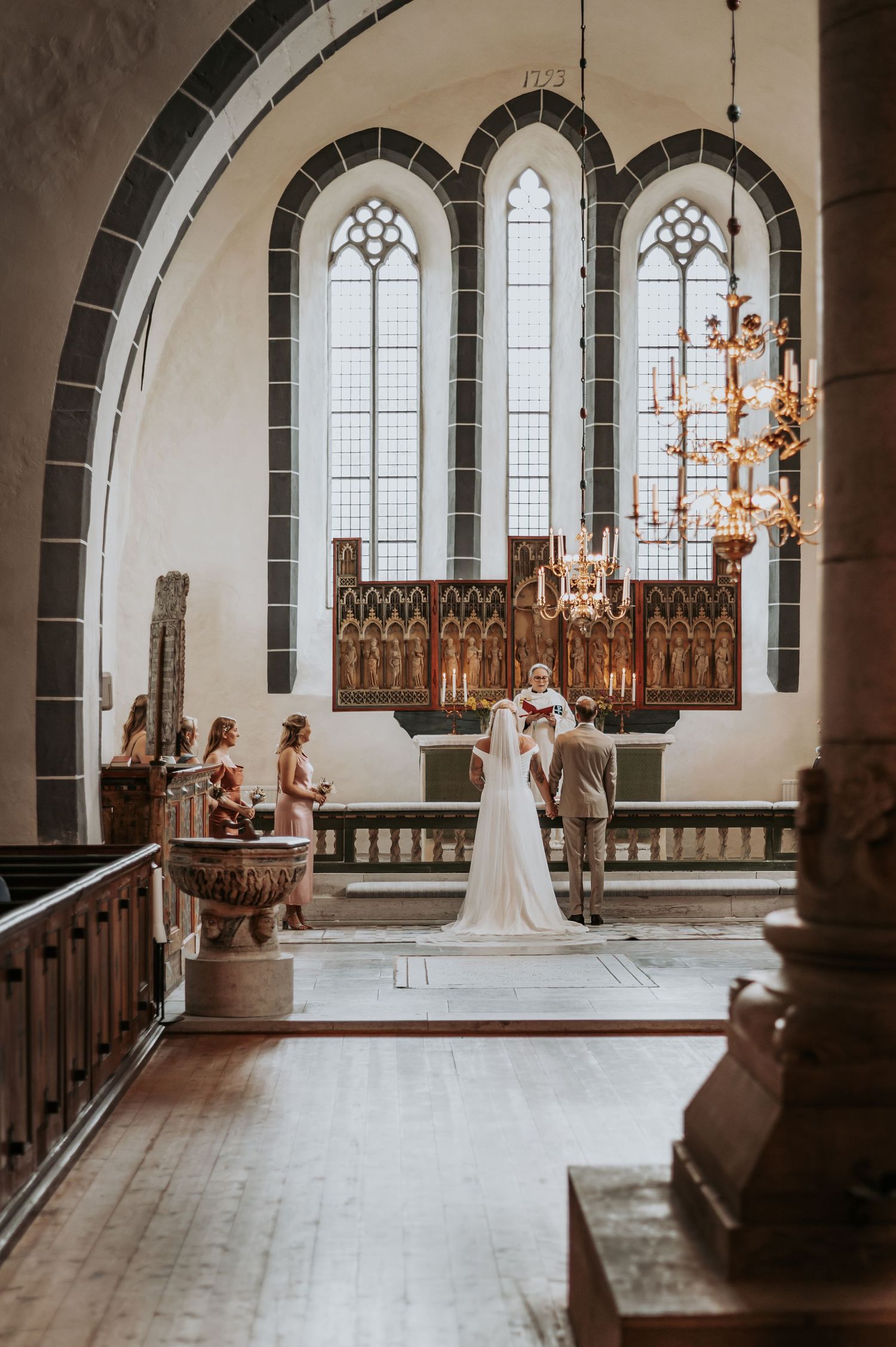 Gothic church interior with arched windows and chandeliers during a wedding ceremony.