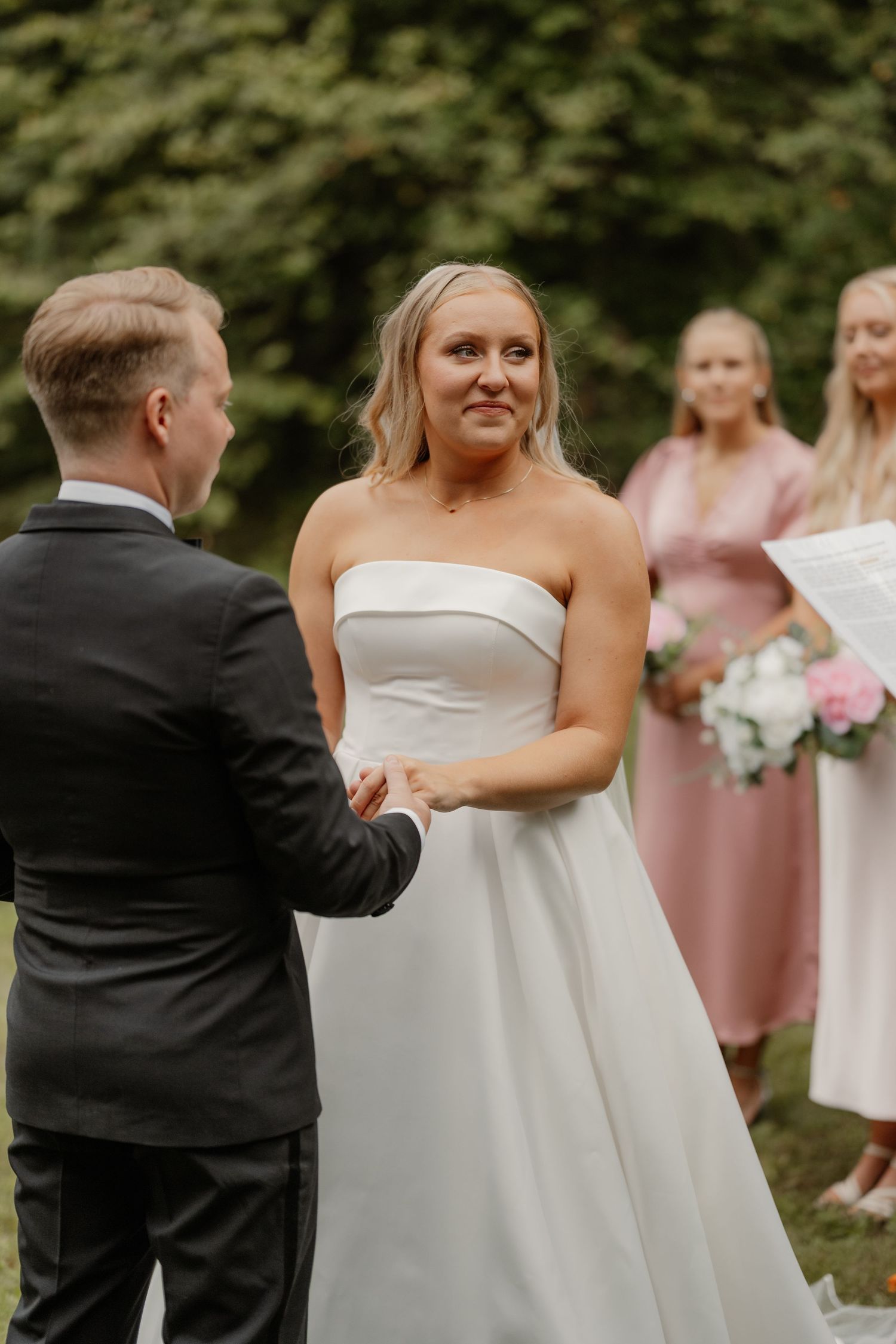 Wedding couple and wedding party in pink dresses share a joyful moment outdoors during photo session.