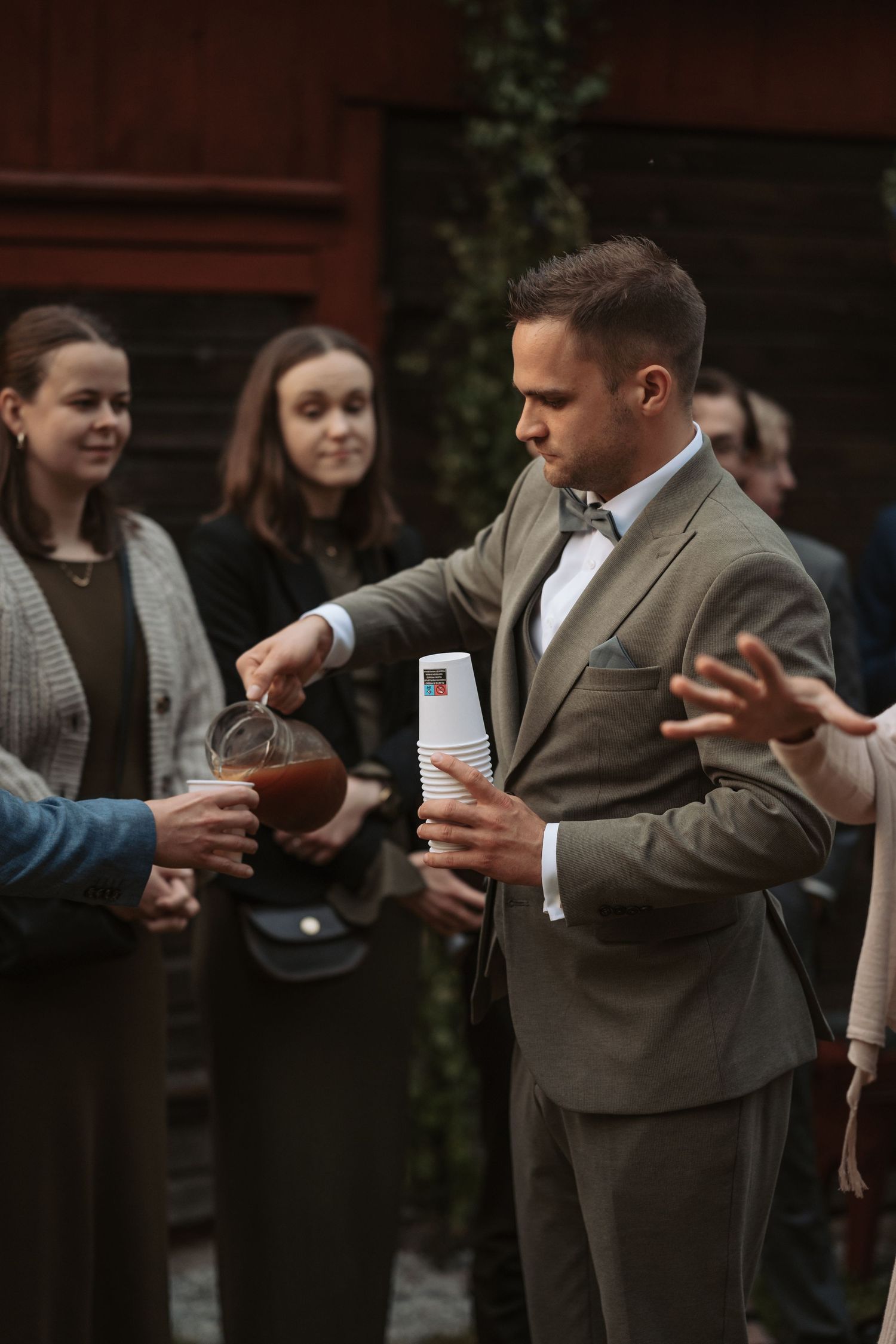 A magician in a gray suit performs card tricks for a small audience during an outdoor event.