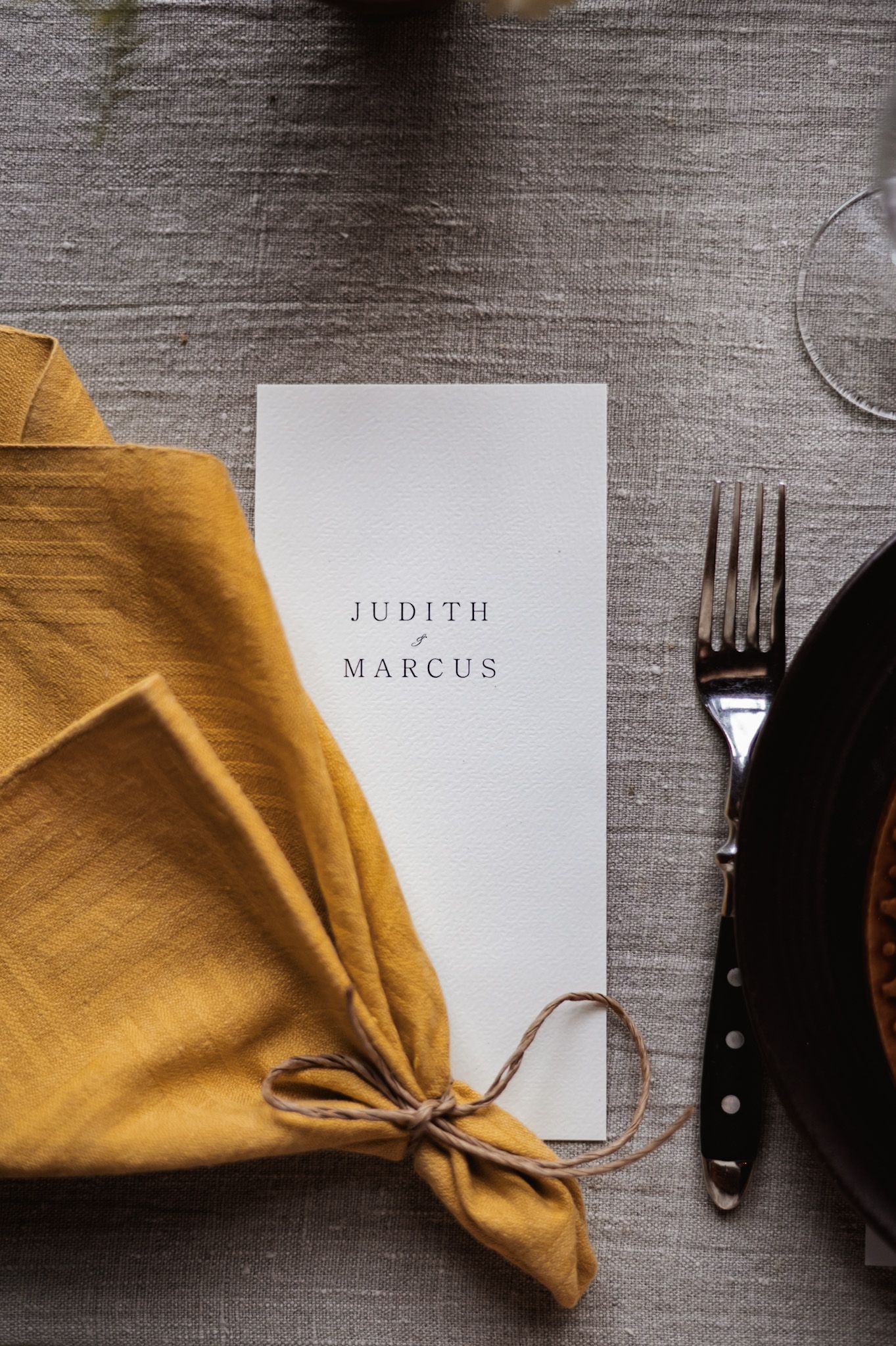 Minimalist wedding menu card with names Judith and Marcus beside yellow napkin.