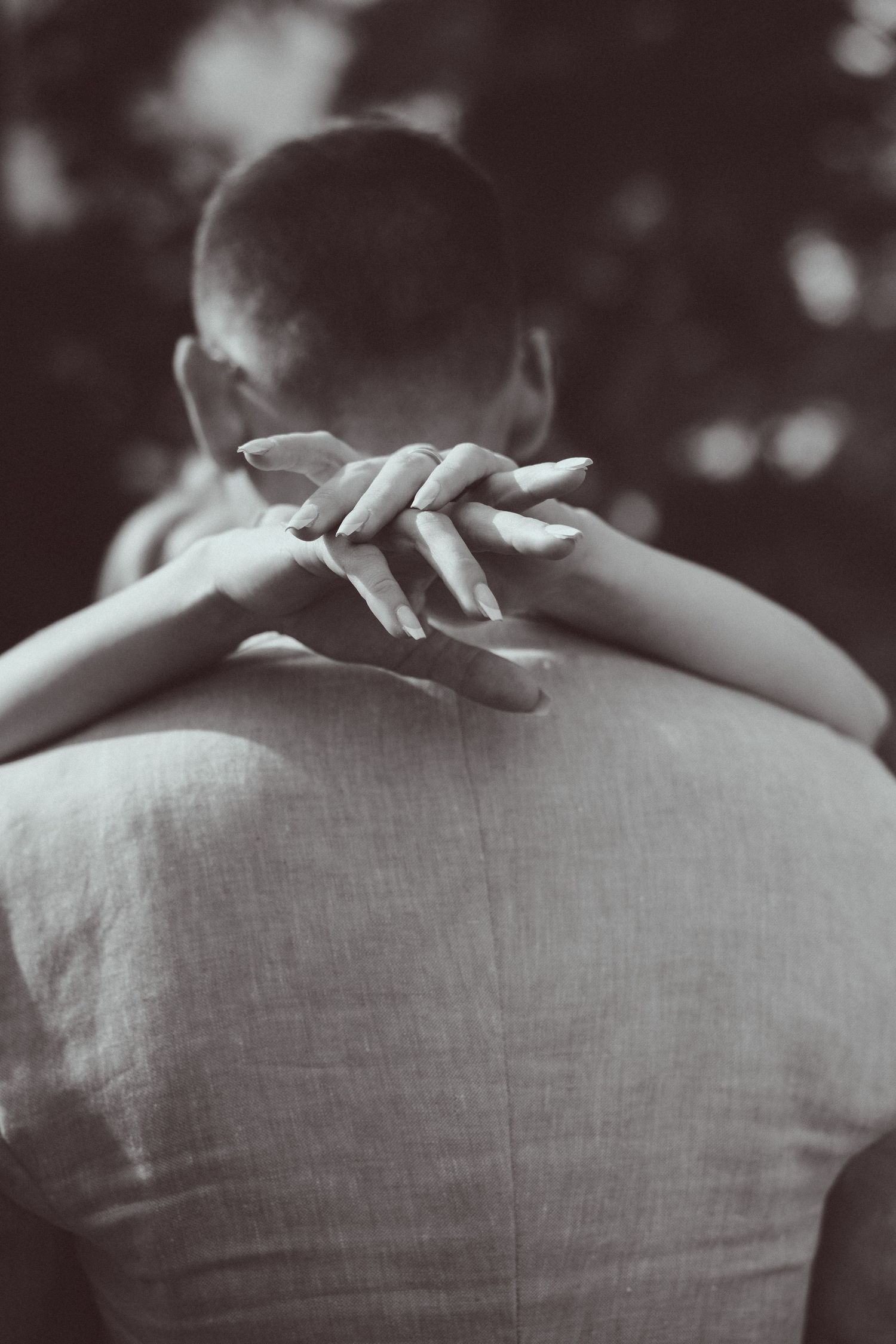 Black and white photo of a person being embraced from behind, with hands clasped around their neck.