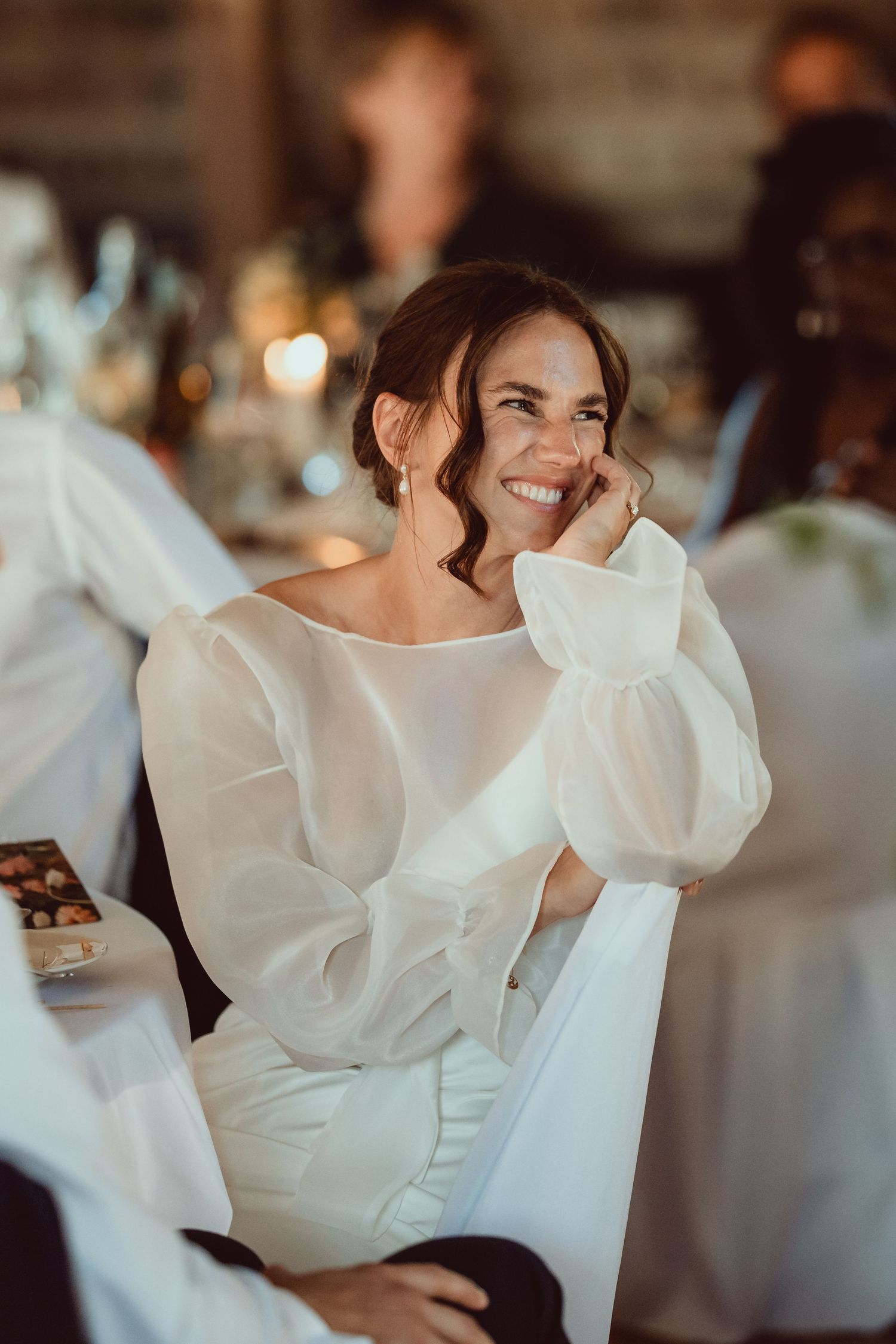 A bride in a modern white wedding dress with dramatic puffy sleeves smiles during a wedding reception.