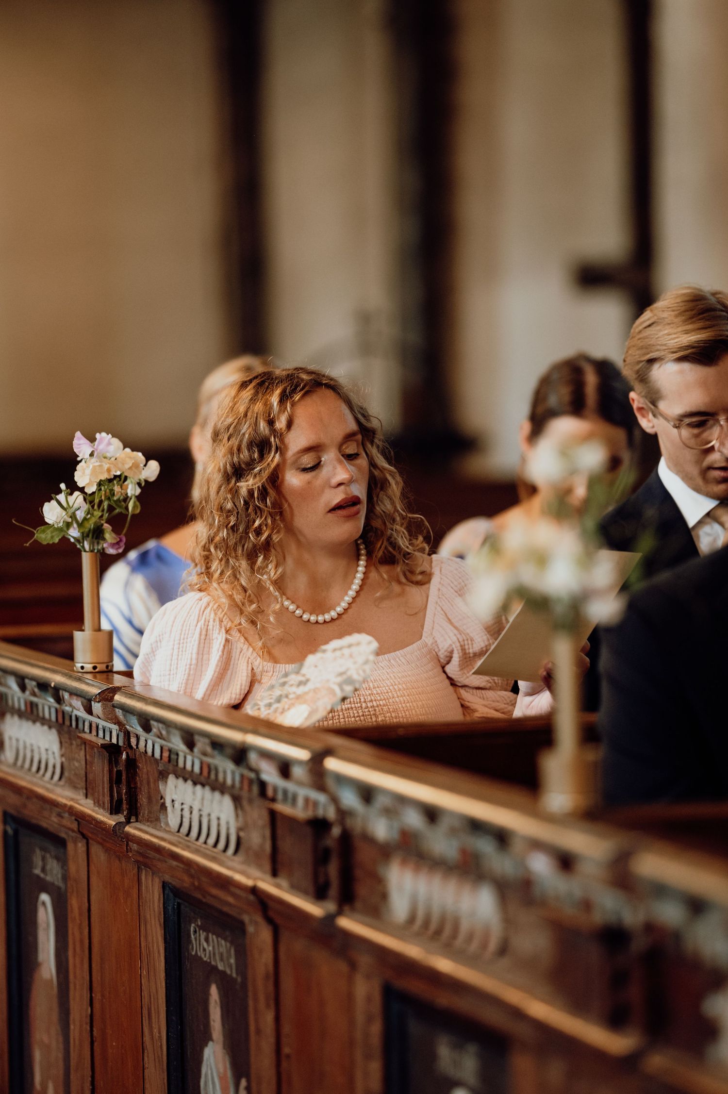 Wedding party members laughing and dancing in wooden church pews during a celebration.