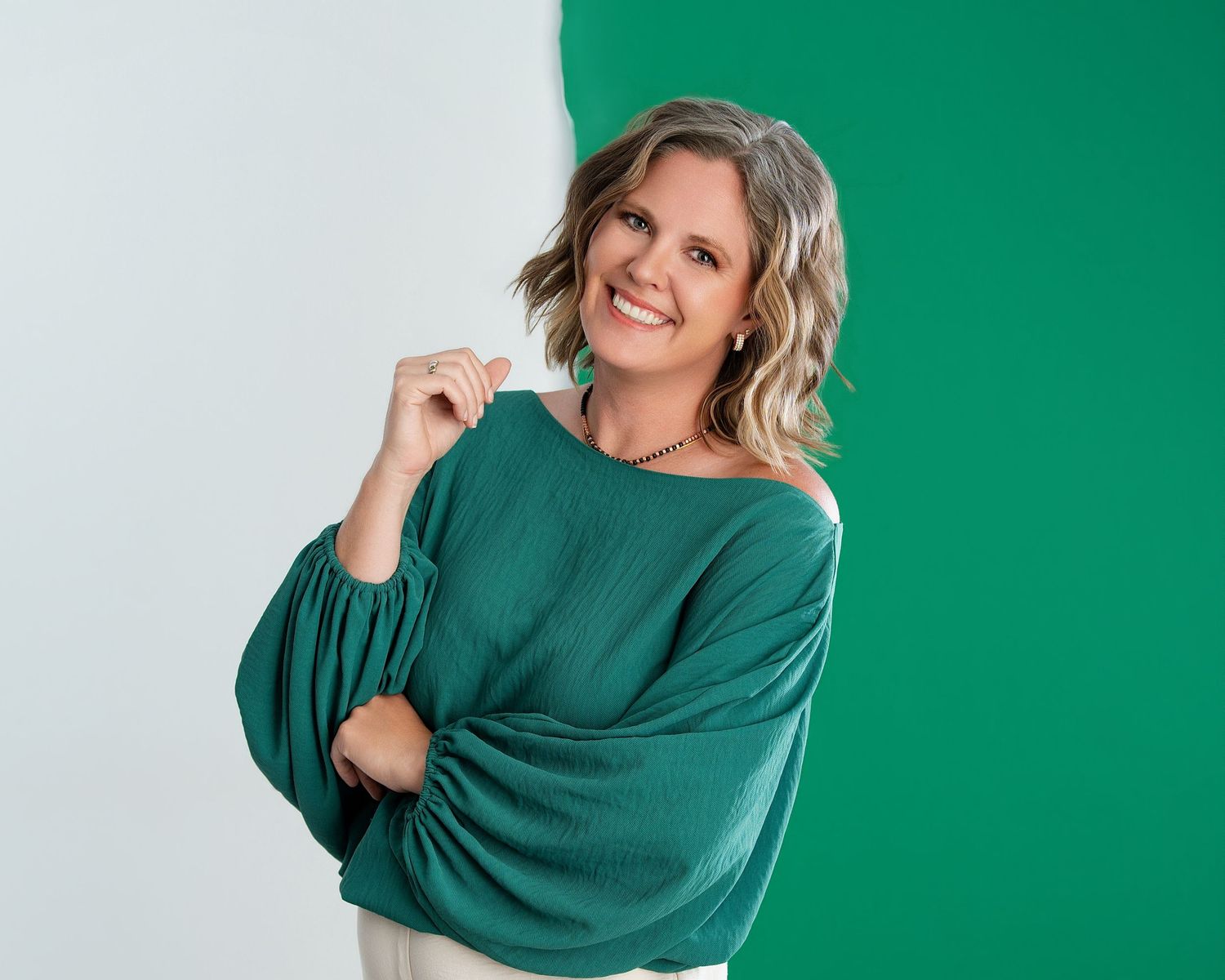 Smiling woman in teal sweater poses confidently against green and white background.