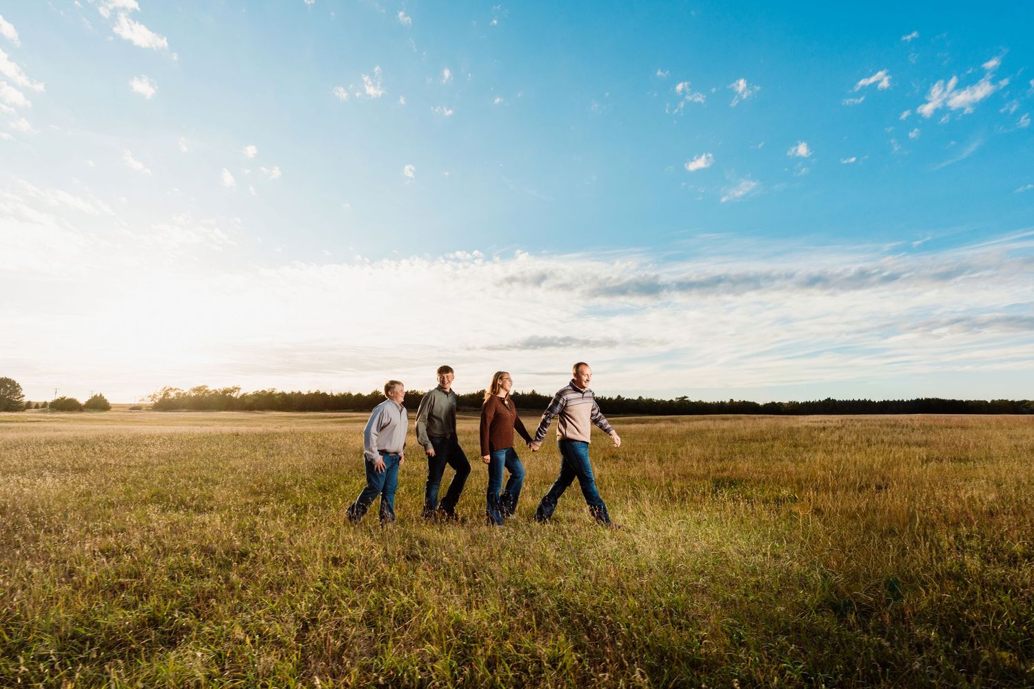 Group of people standing together in a golden wheat field under bright blue sky during sunset.