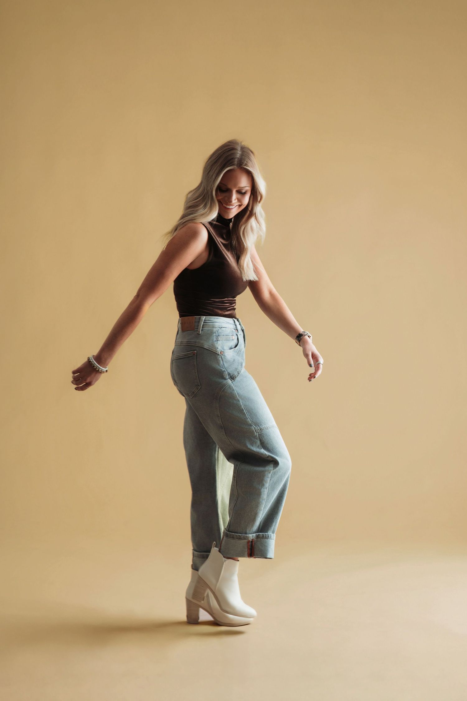 Dancer performs dynamic breakdancing moves in casual jeans and tank top against beige background.
