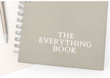 A gray spiral-bound notebook titled 'The Everything Book' resting on a notepad with a pen beside it.