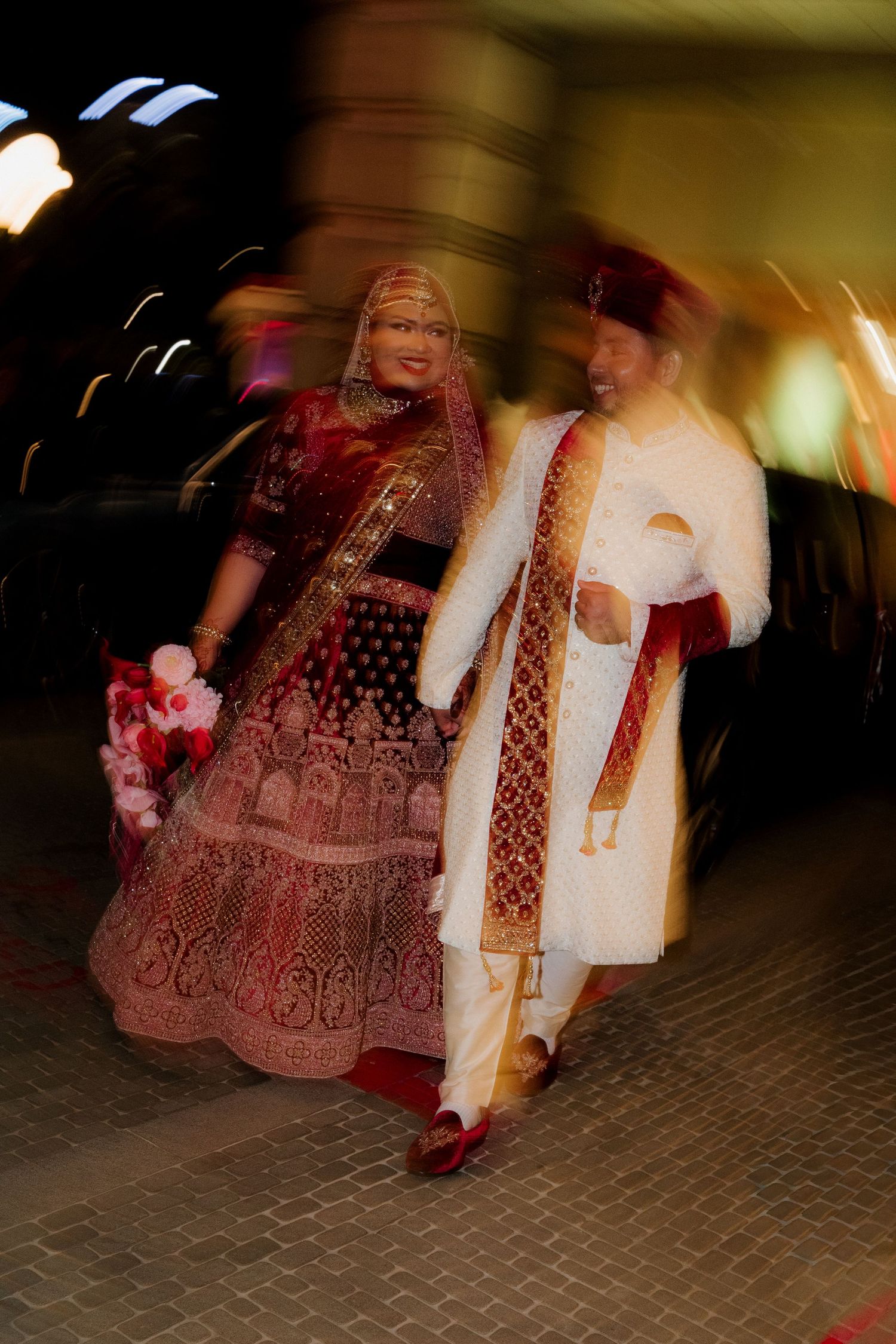 Indian bride and groom in traditional wedding attire walking together at night, captured with motion blur effect.