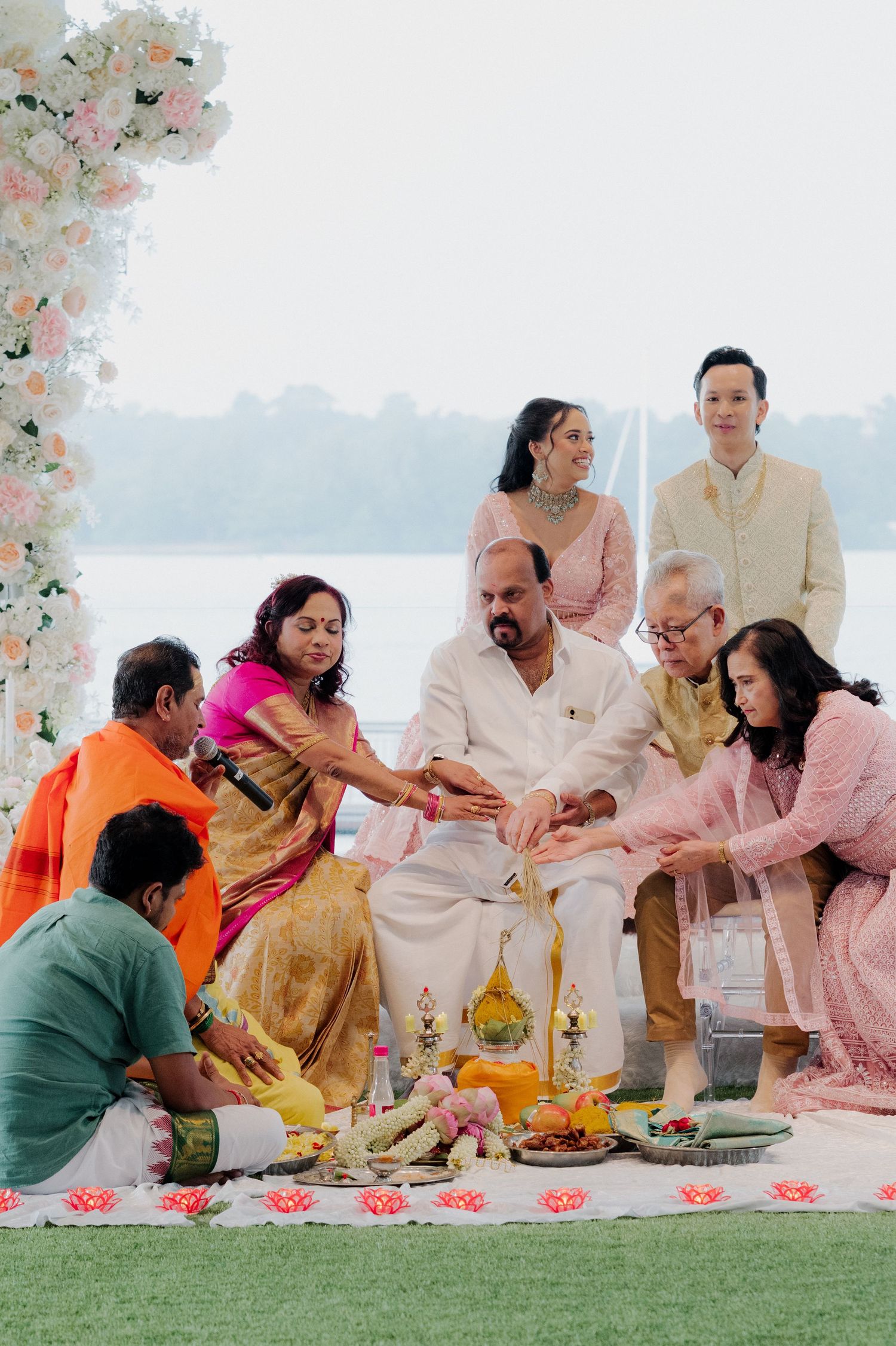 Family gathered for a traditional Indian wedding ceremony outdoors, wearing colorful sarees and kurtas near a floral backdrop.
