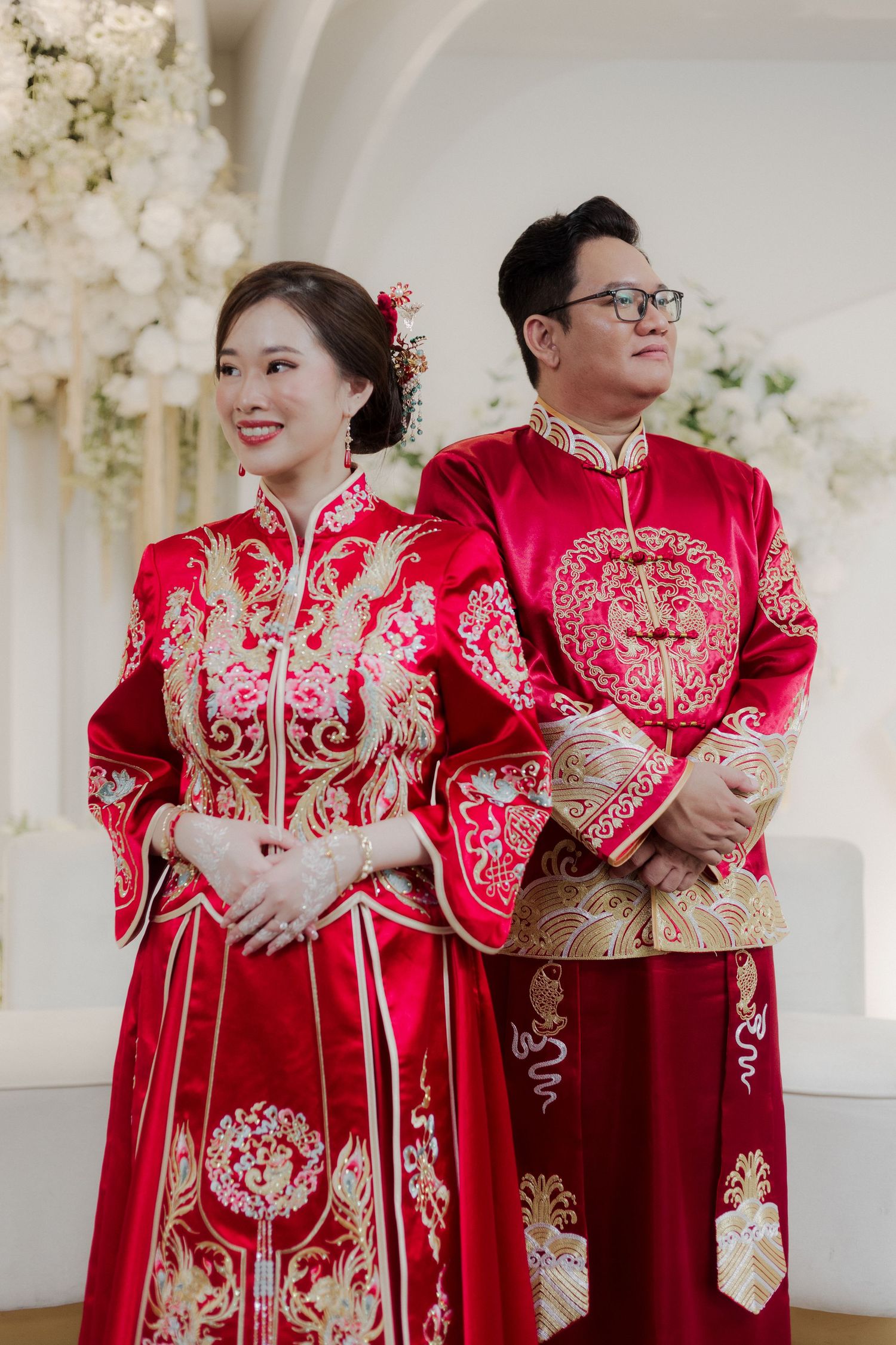 Couple in traditional red and gold Chinese wedding attire, qipao and tangzhuang, posing elegantly at a formal ceremony.