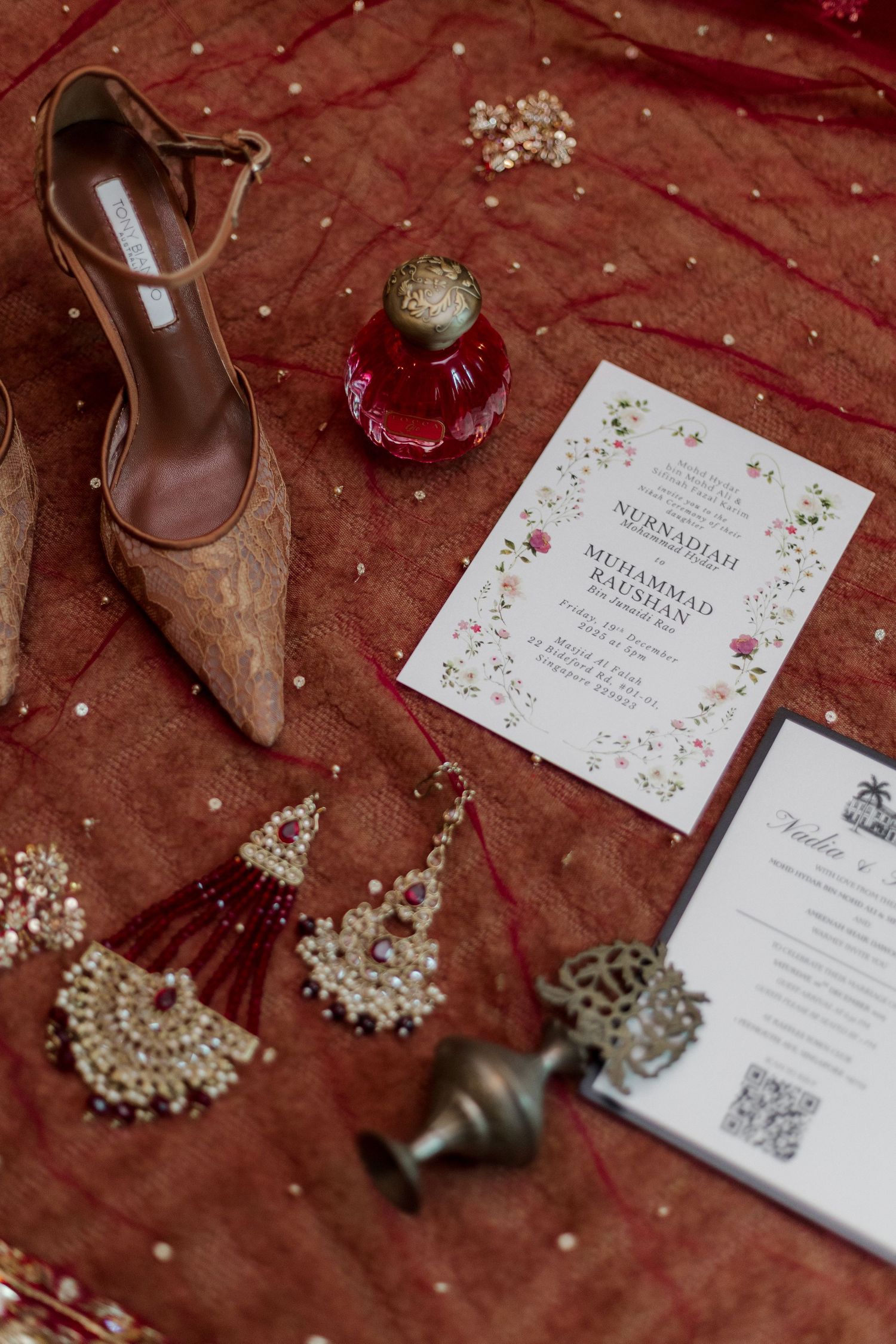 Elegant South Asian bridal flat lay with embroidered heels, chandelier earrings, red perfume bottle, and floral wedding invitation.