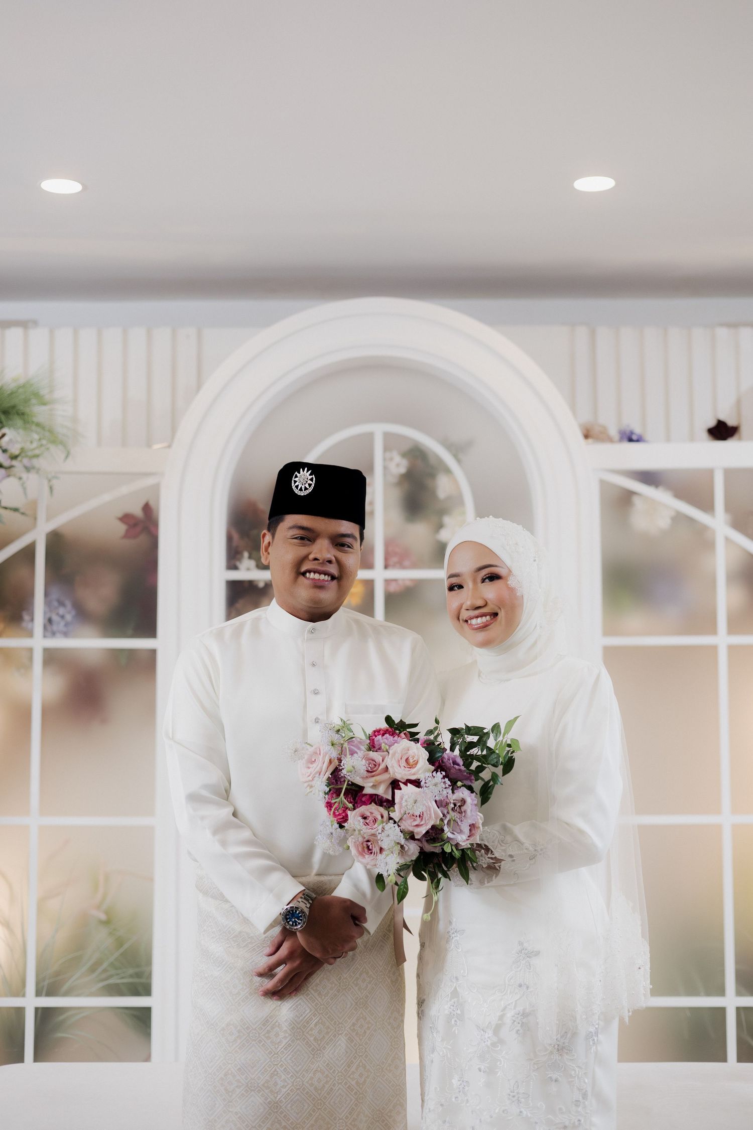A joyful wedding couple in white traditional attire share laughter and smiles during their ceremony.