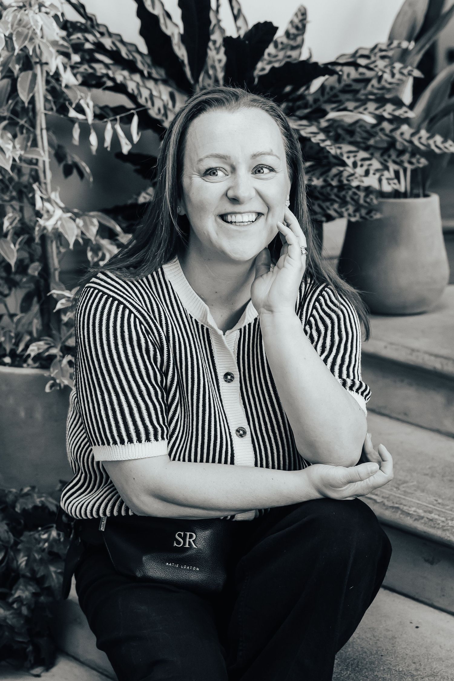 Black and white portrait of Sophie Ruck in striped shirt seated among lush potted plants.