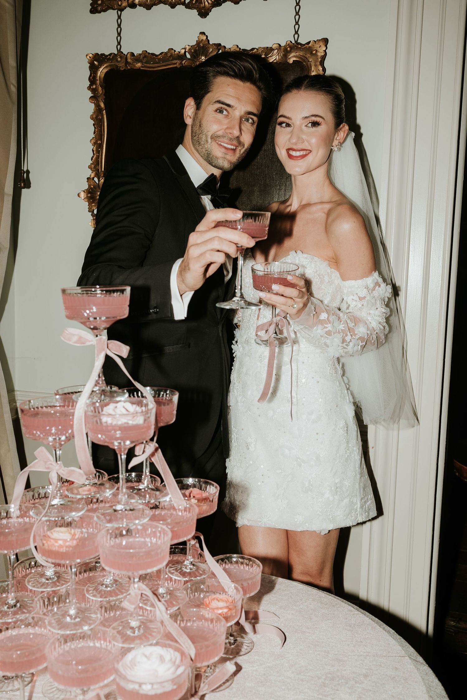Editorial flash photograph-Couple posed in front of pink cocktail tower. Bride in stylish short dress. Prestwold hall