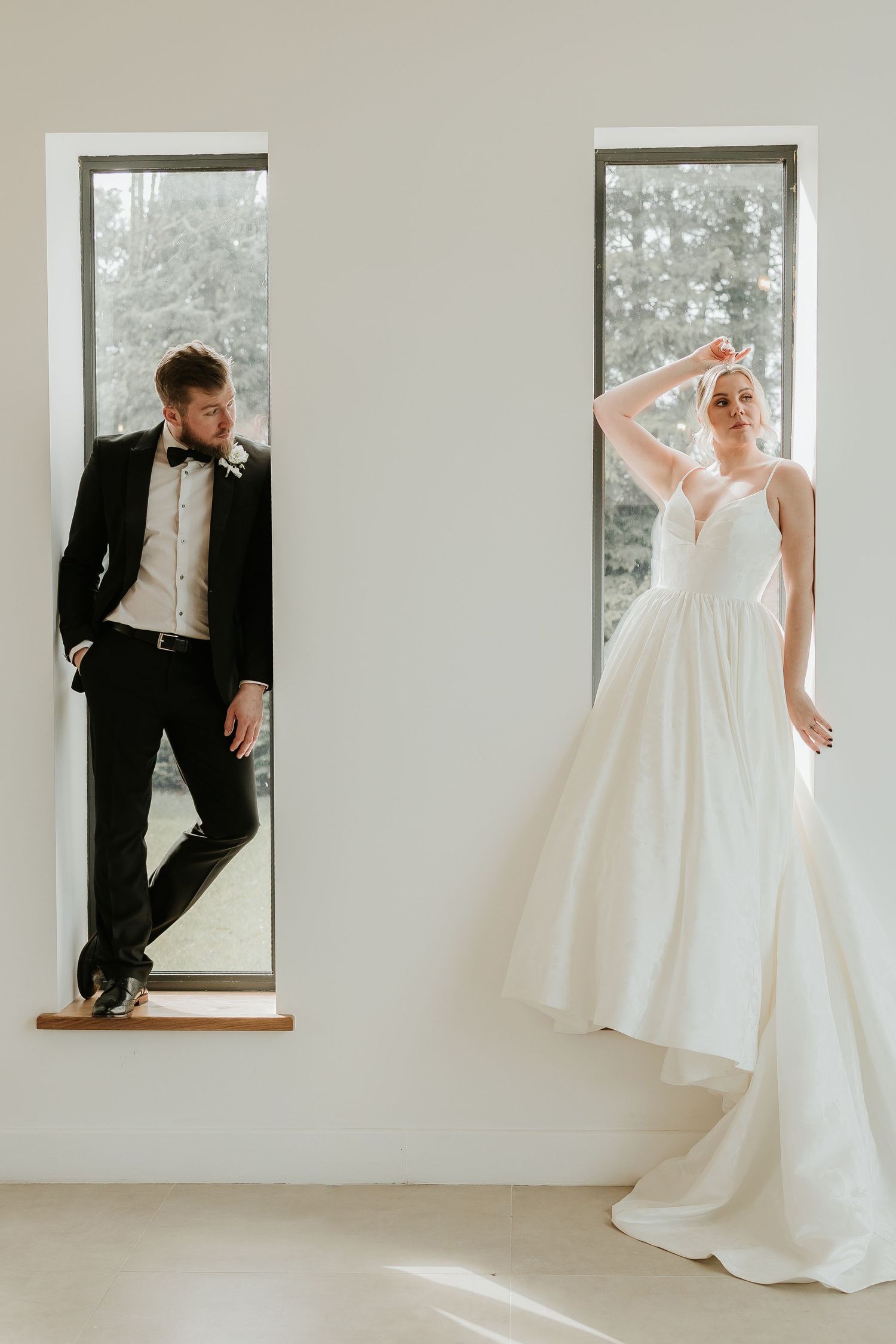 A minimalist wedding photo series showing the couple posing playfully in white windows of a bright modern space.