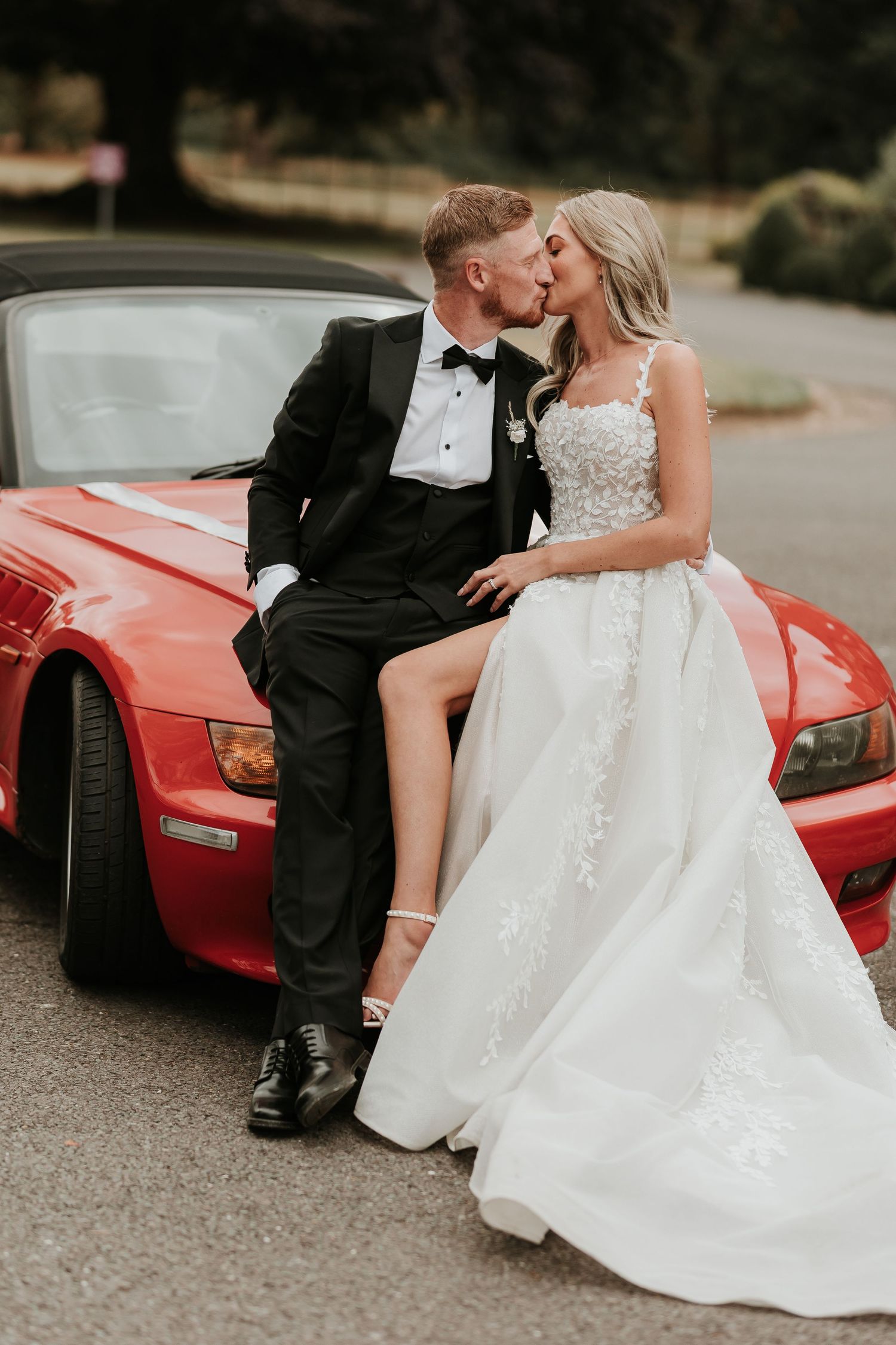 A romantic wedding photo series showing a couple in formal attire posing with a red sports car.