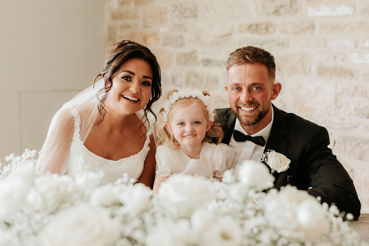 A romantic wedding photo collage showing multiple angles of a bride and groom embracing among white floral decorations.