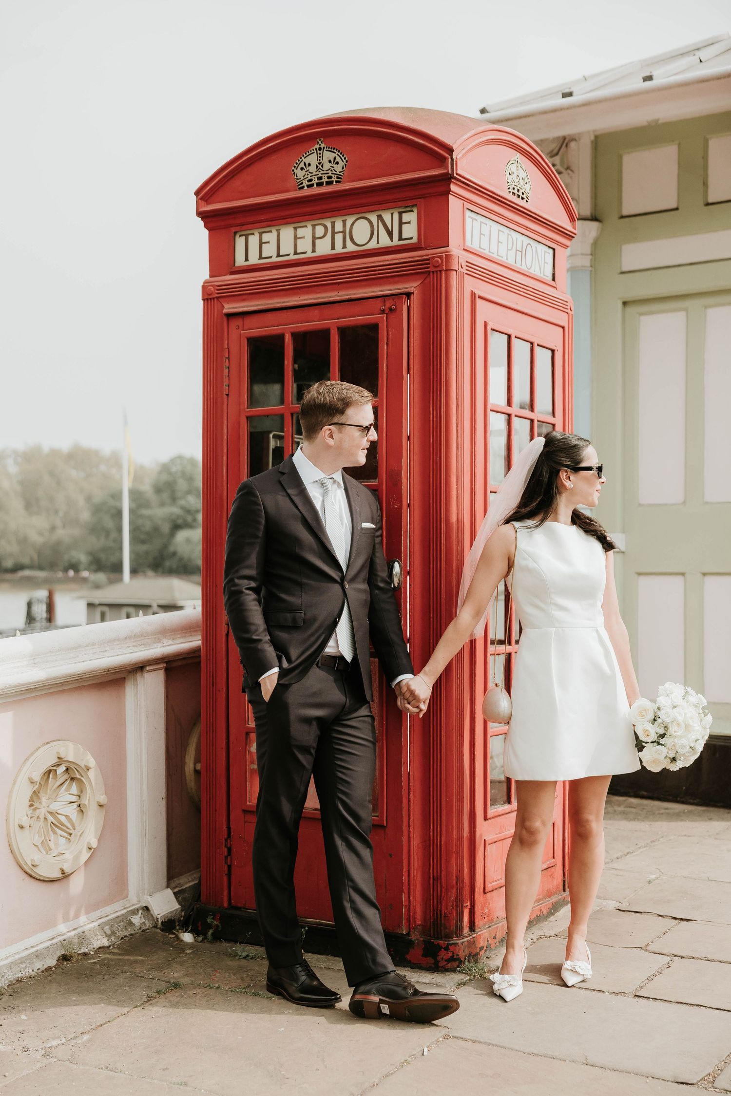 A series of romantic wedding photos featuring a couple posing playfully with a classic red British telephone booth.