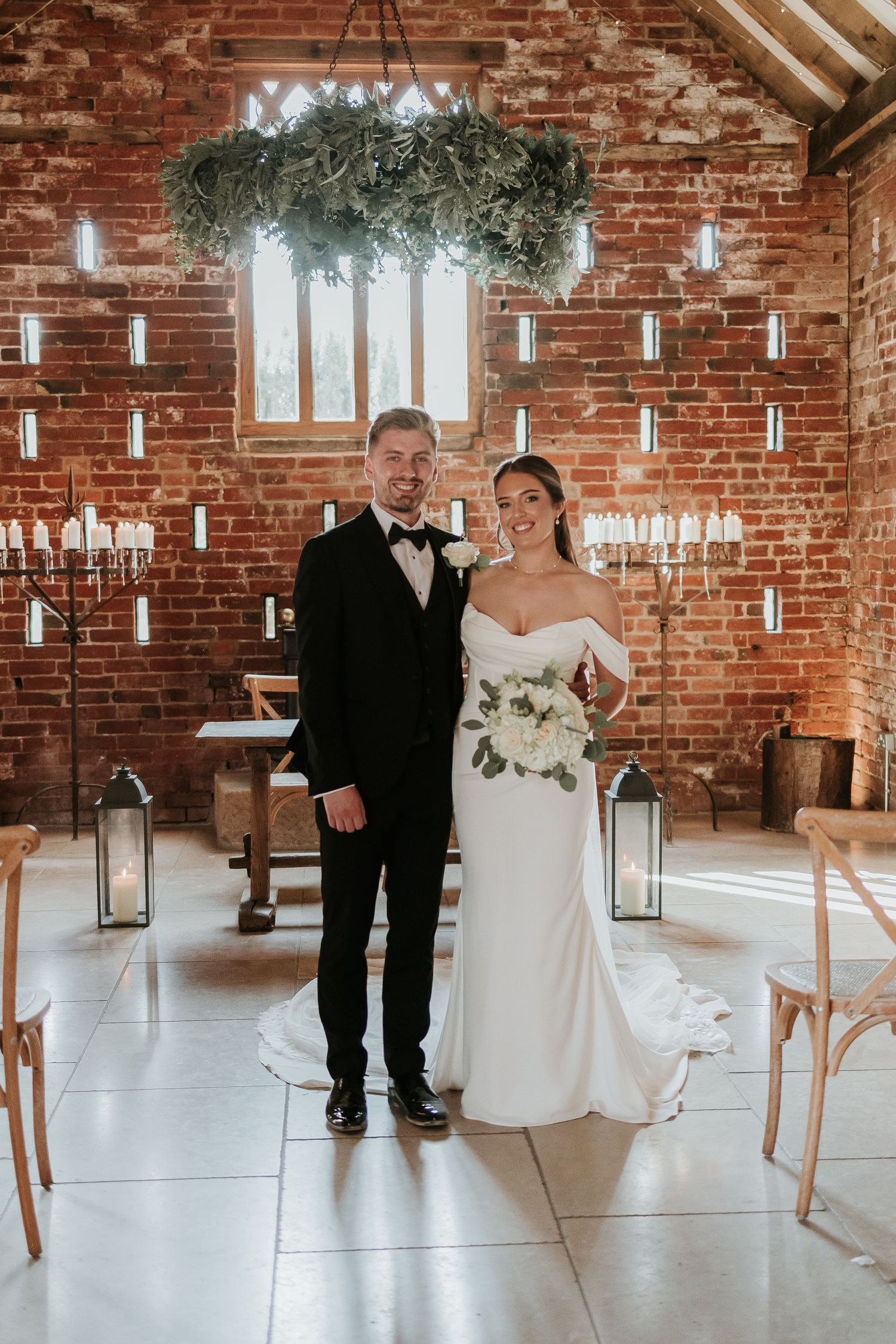 Black and white wedding ceremony scene in rustic brick venue with natural light streaming through windows.