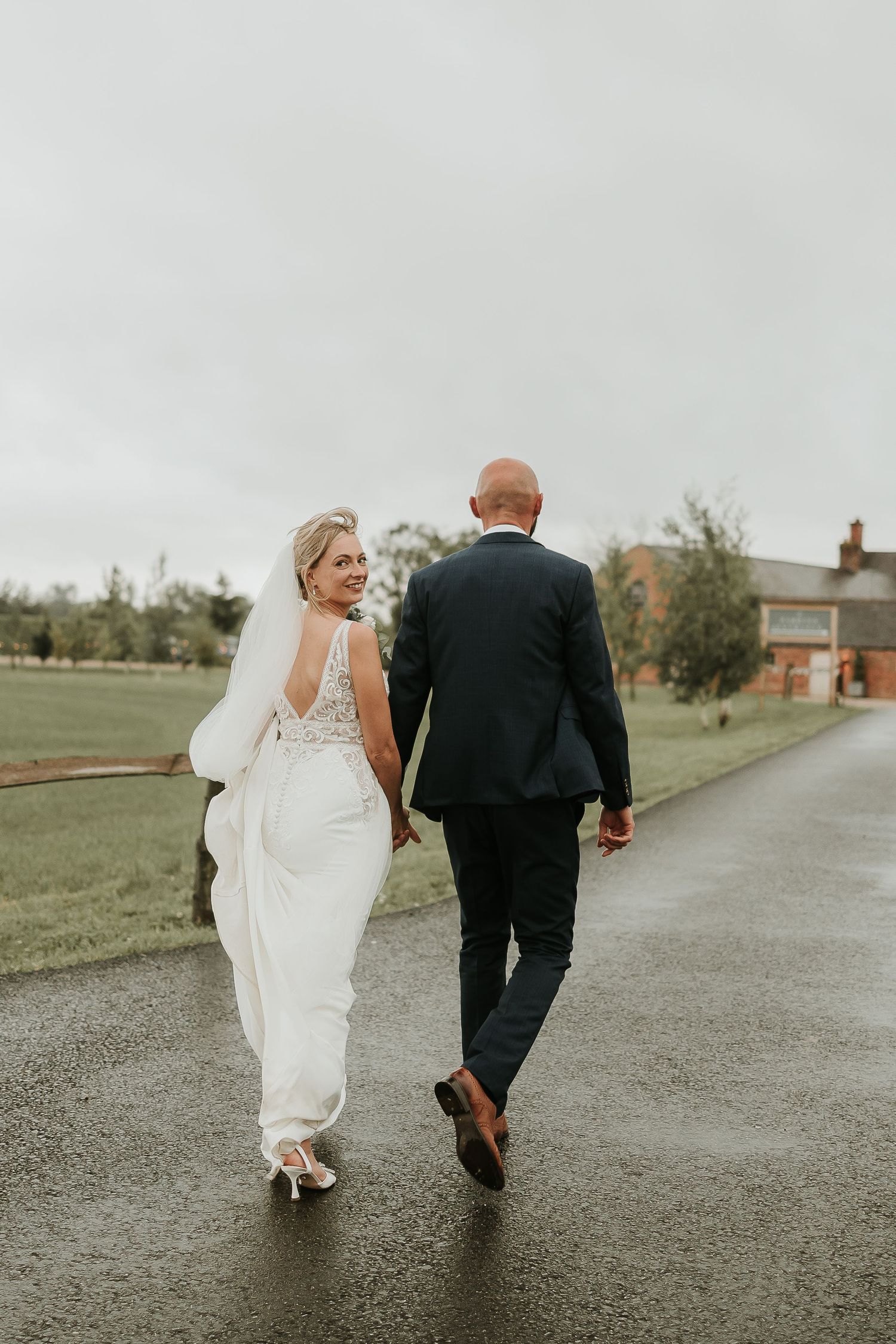 A couple in wedding attire walking away on a rainy path.