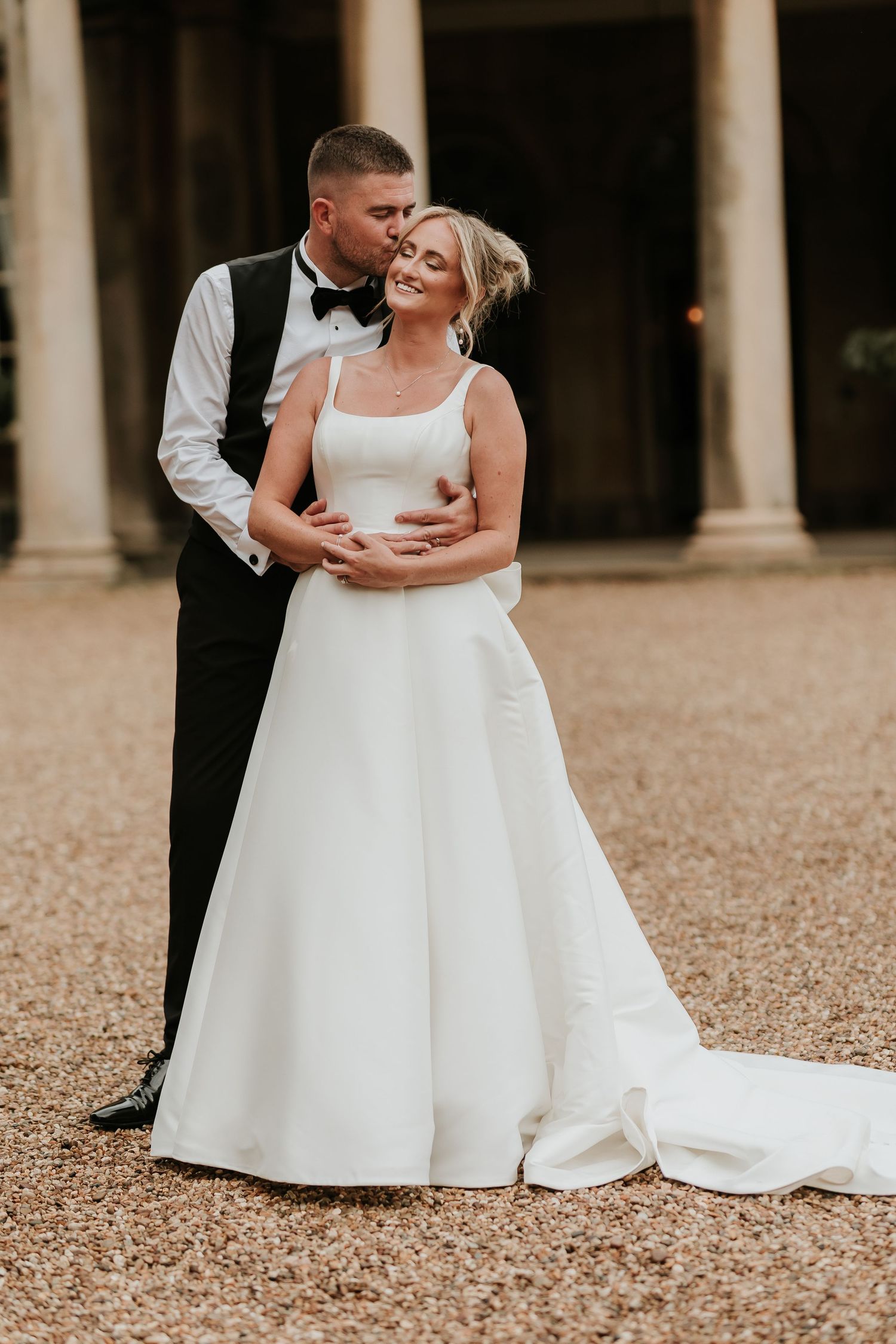A couple in wedding attire share an intimate dance together outdoors near classical stone columns.