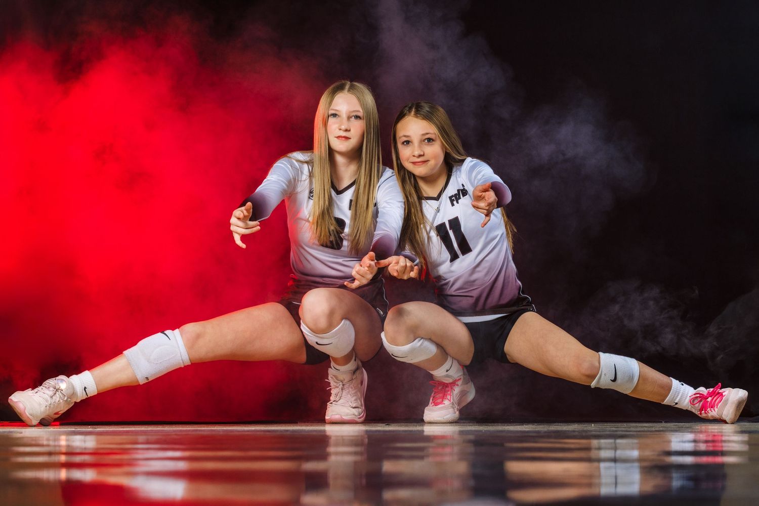 Two volleyball players in white uniforms dive for the ball during an intense match on the court.