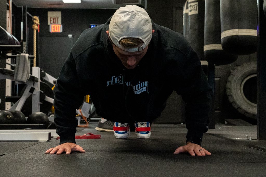 Brands portrait of a gym goer wearing a black hoodie and white had doing pushups.