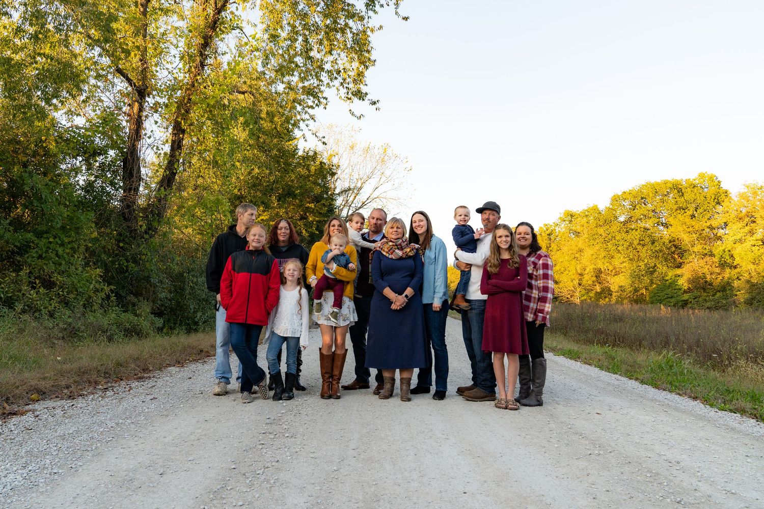 Family portrait of a large group including grandma, kids and grandkids standing on a rock road with fall leaves in the background.