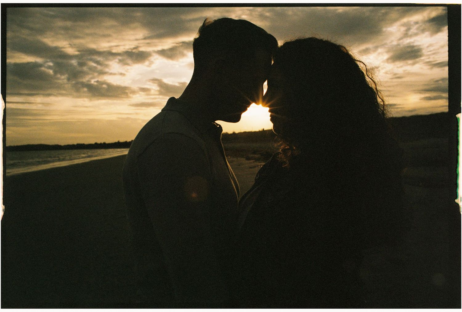 Silhouetted couple in an intimate moment against a dramatic sunset sky over the ocean.
