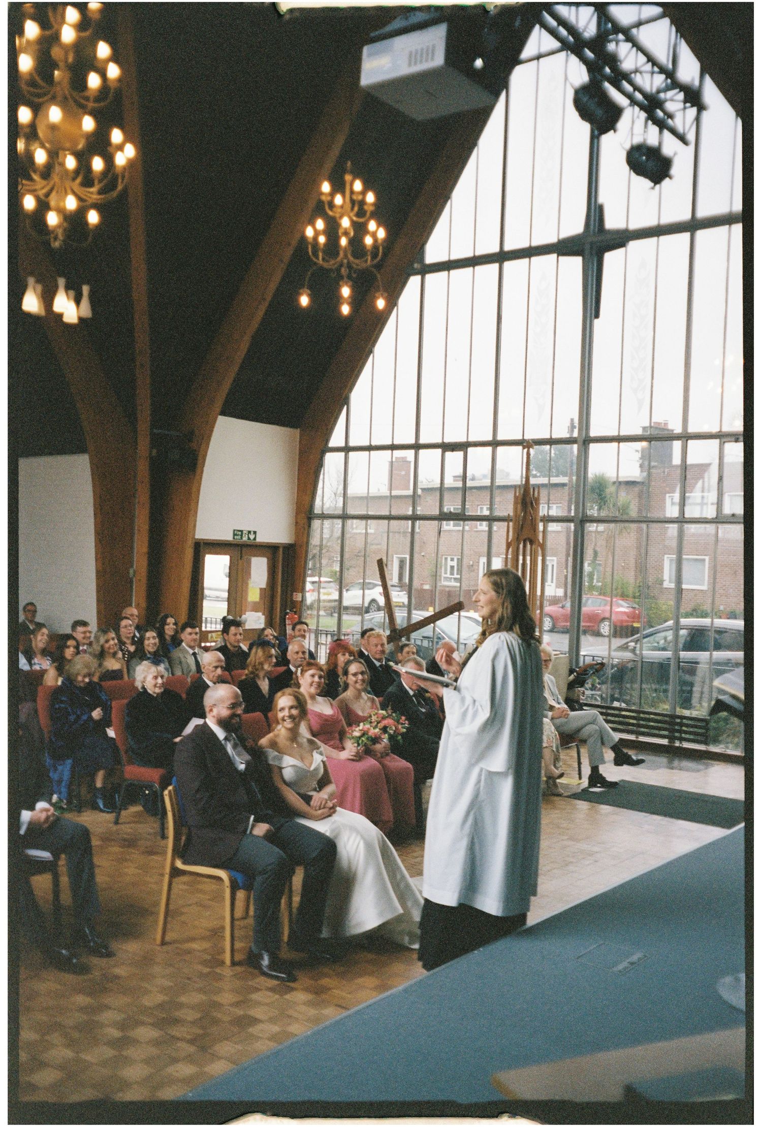 Church congregation gathered in a modern chapel with wooden beams and chandeliers during a service.