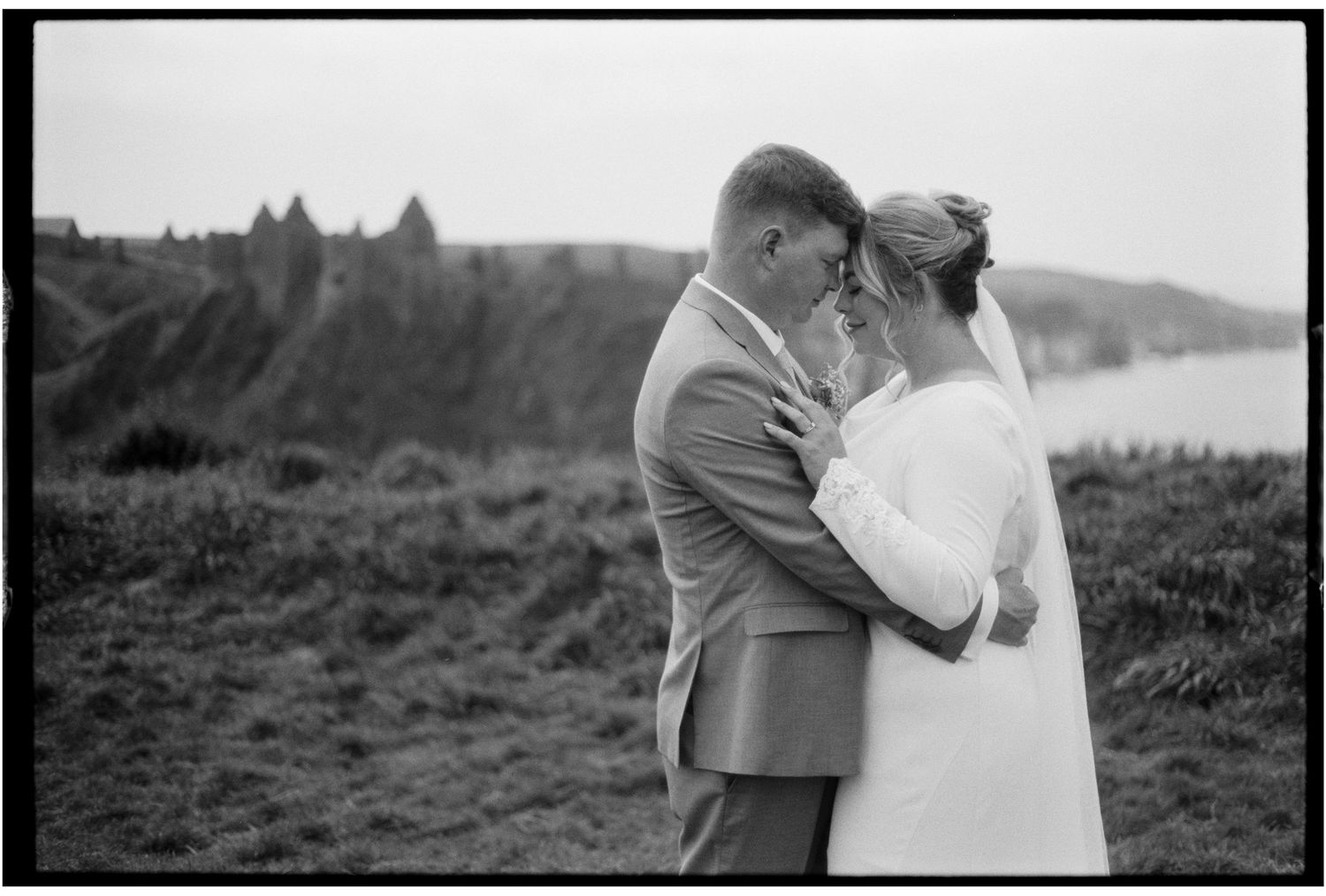 A black and white romantic photo of a couple embracing on a misty hilltop in nature.