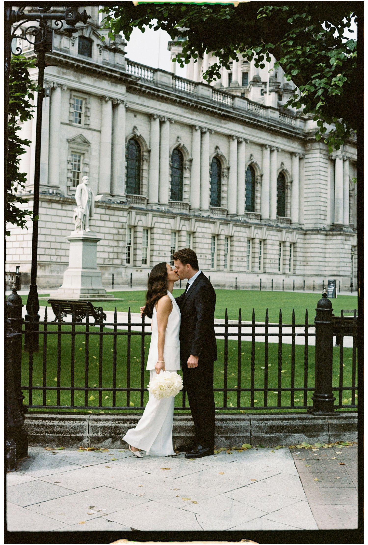 Couple poses for romantic wedding photos in front of an elegant historic building with iron gates.