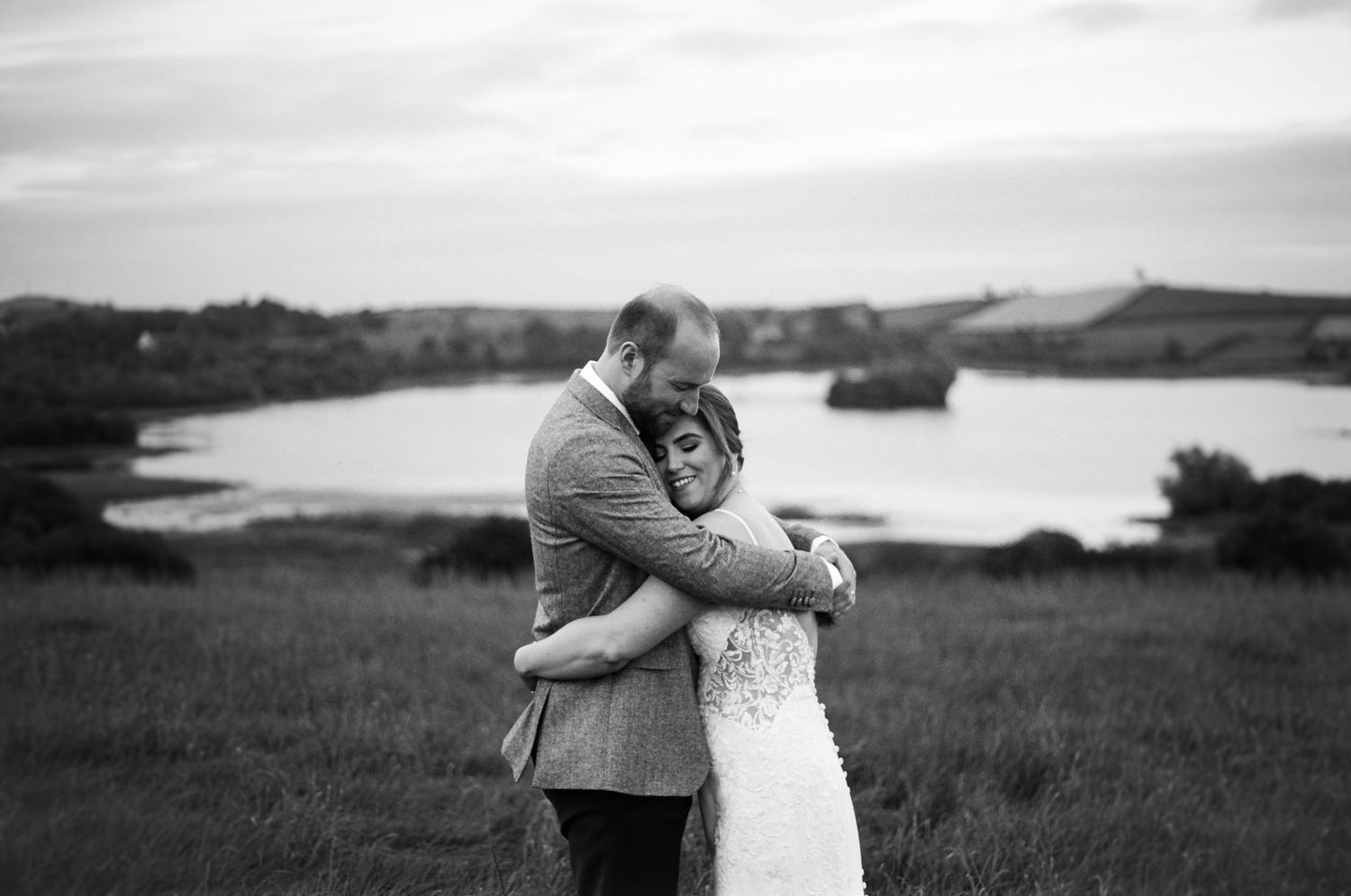 Black and white wedding photos showing romantic couples embracing in scenic outdoor settings by the water and fields.