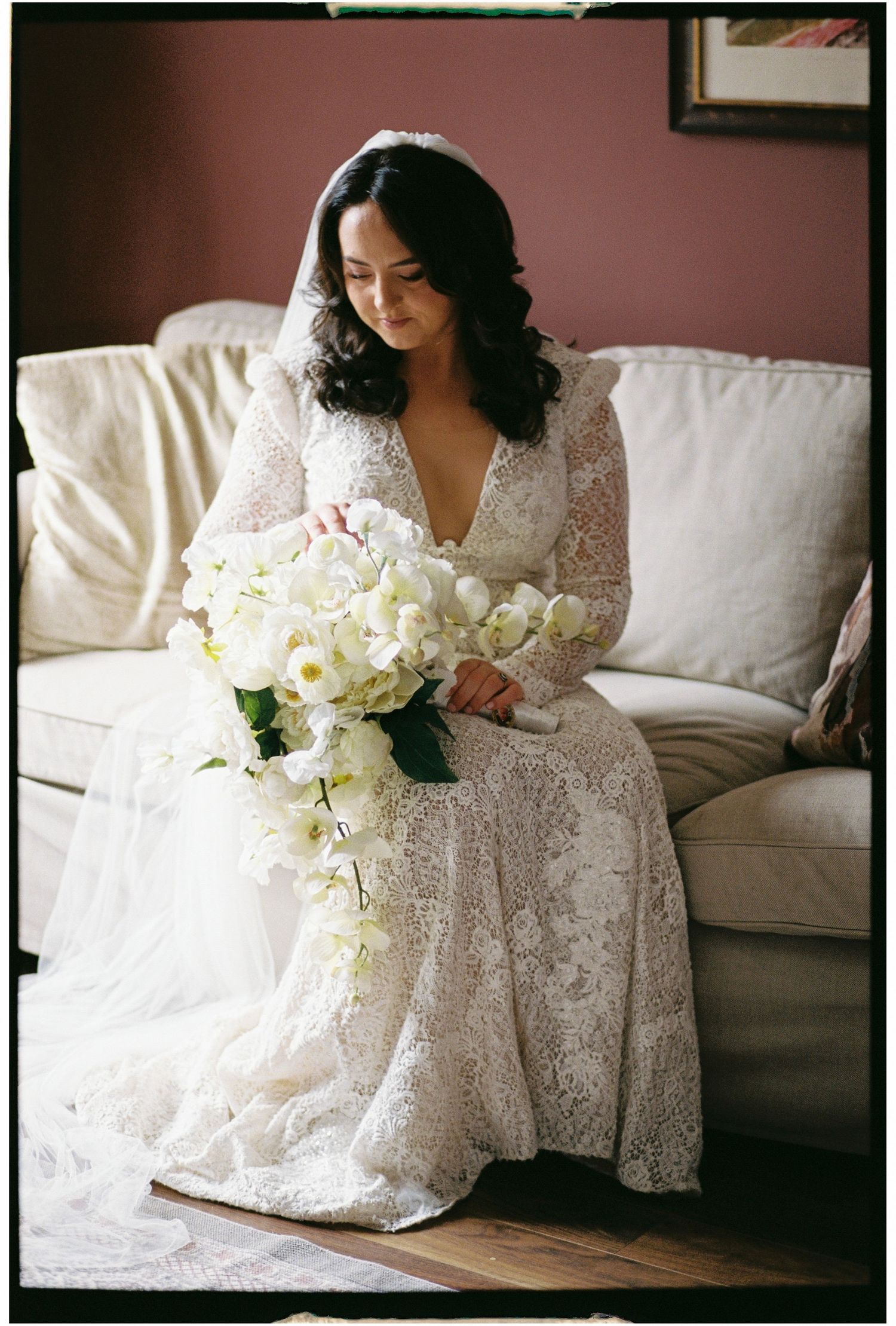 Elegant white lace wedding dress with bouquet of white flowers on a cream colored couch.