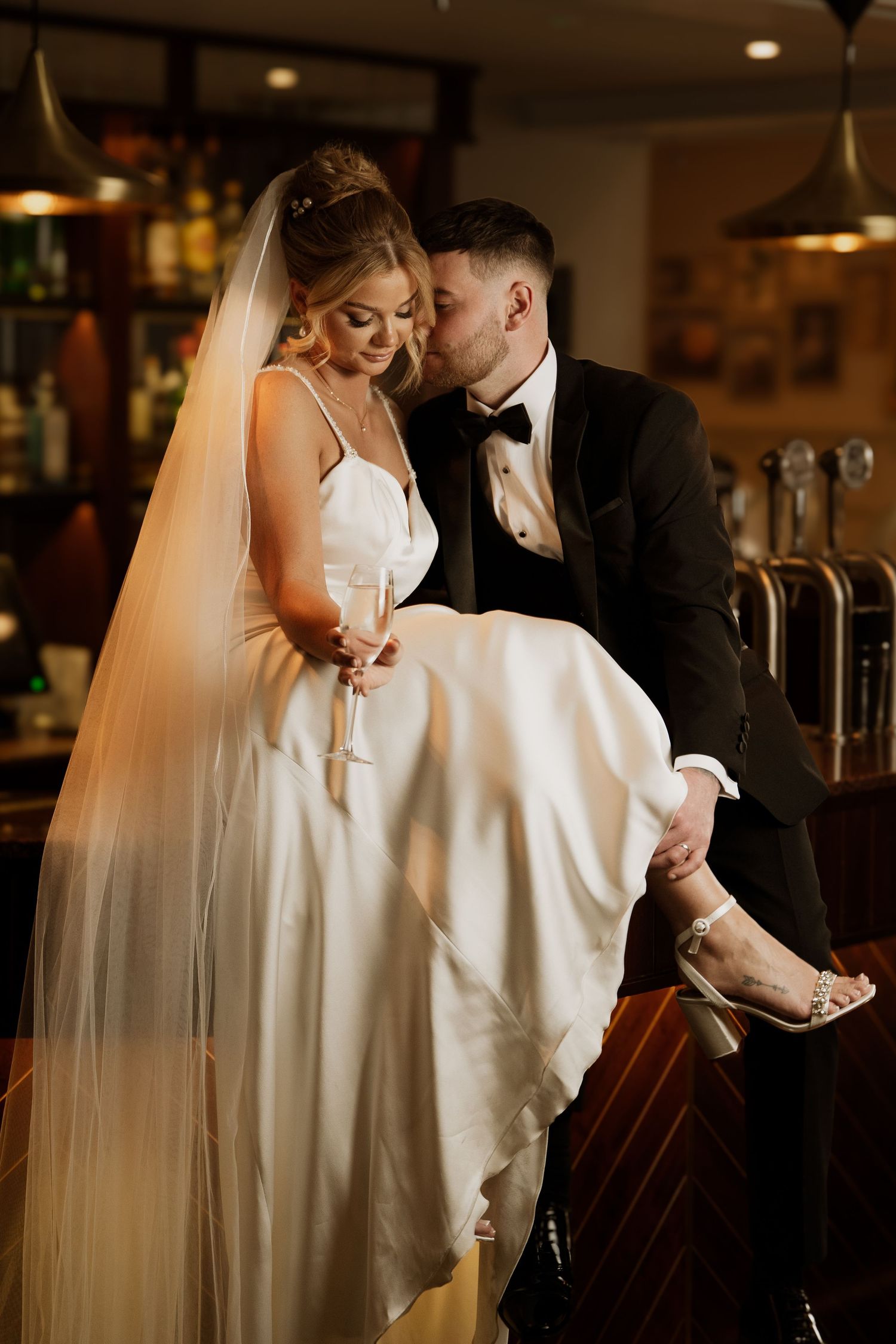 Wedding couple in formal attire shares intimate moments in a warmly lit bar setting.